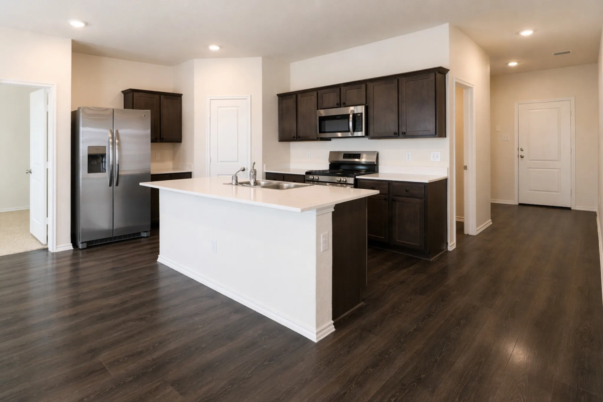 Modern kitchen featuring a central island with an undermount sink, dark wood cabinetry, stainless steel appliances, and wood-finish flooring