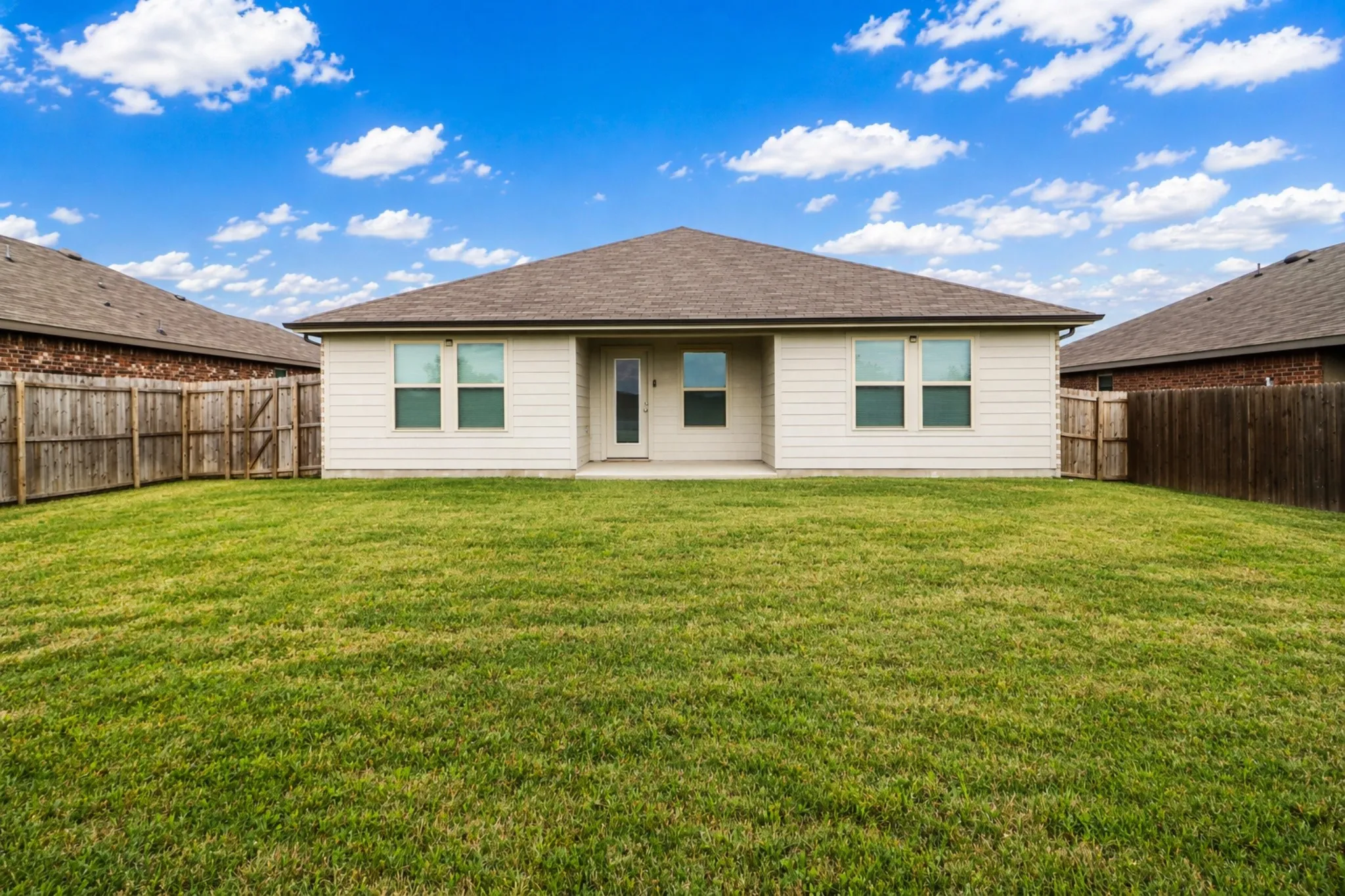 Rear exterior featuring a spacious lawn, covered patio, and privacy fencing
