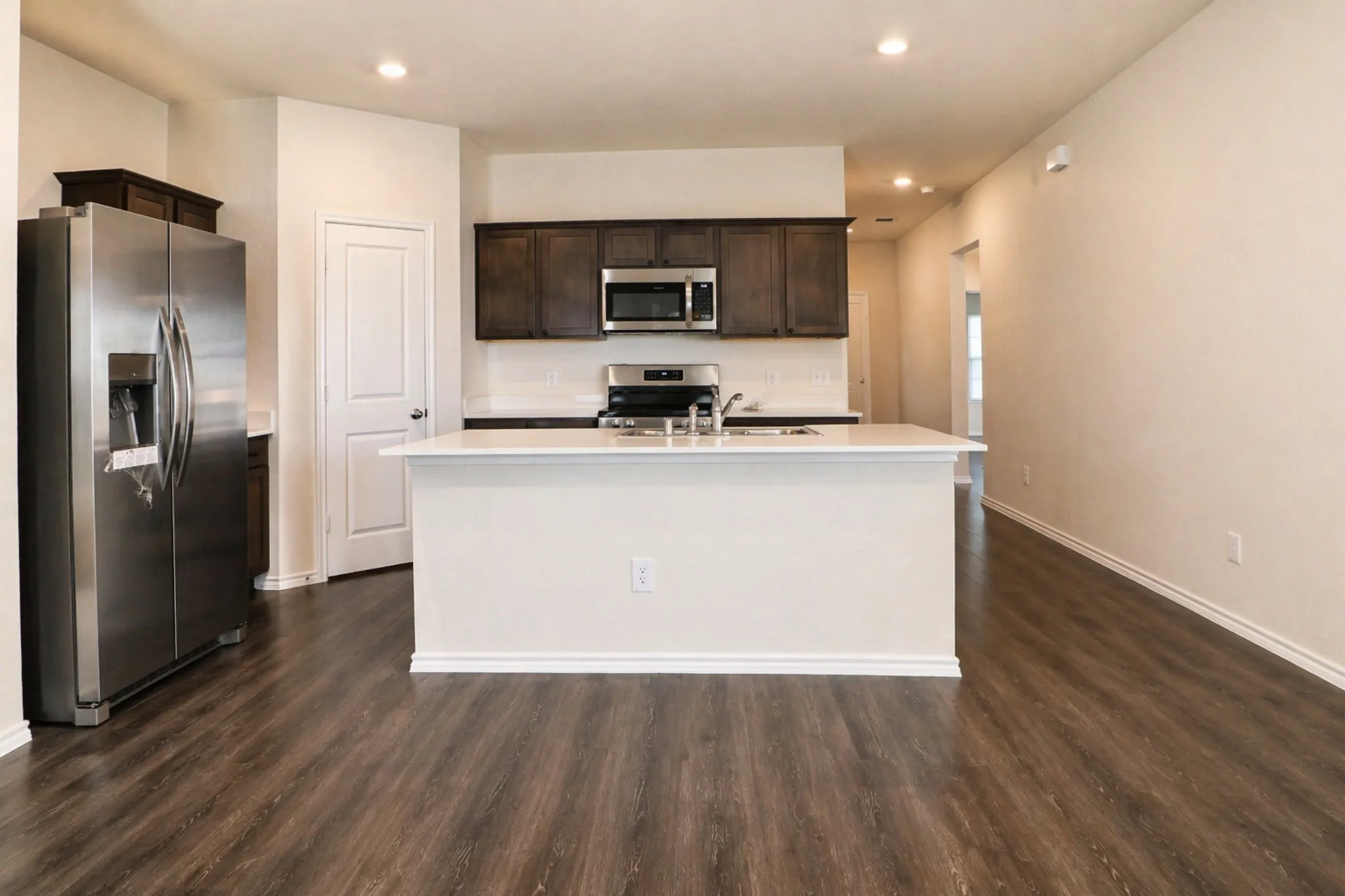 Spacious kitchen featuring dark wood cabinetry, stainless steel appliances, white subway tile backsplash, and a large central island with a white countertop