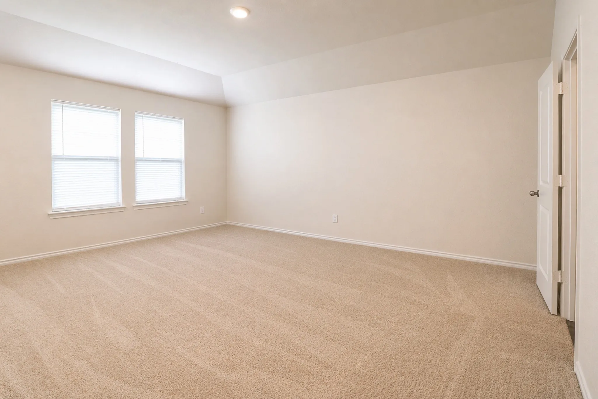 Spacious room featuring neutral carpeting, two windows with blinds, a vaulted ceiling, and recessed lighting