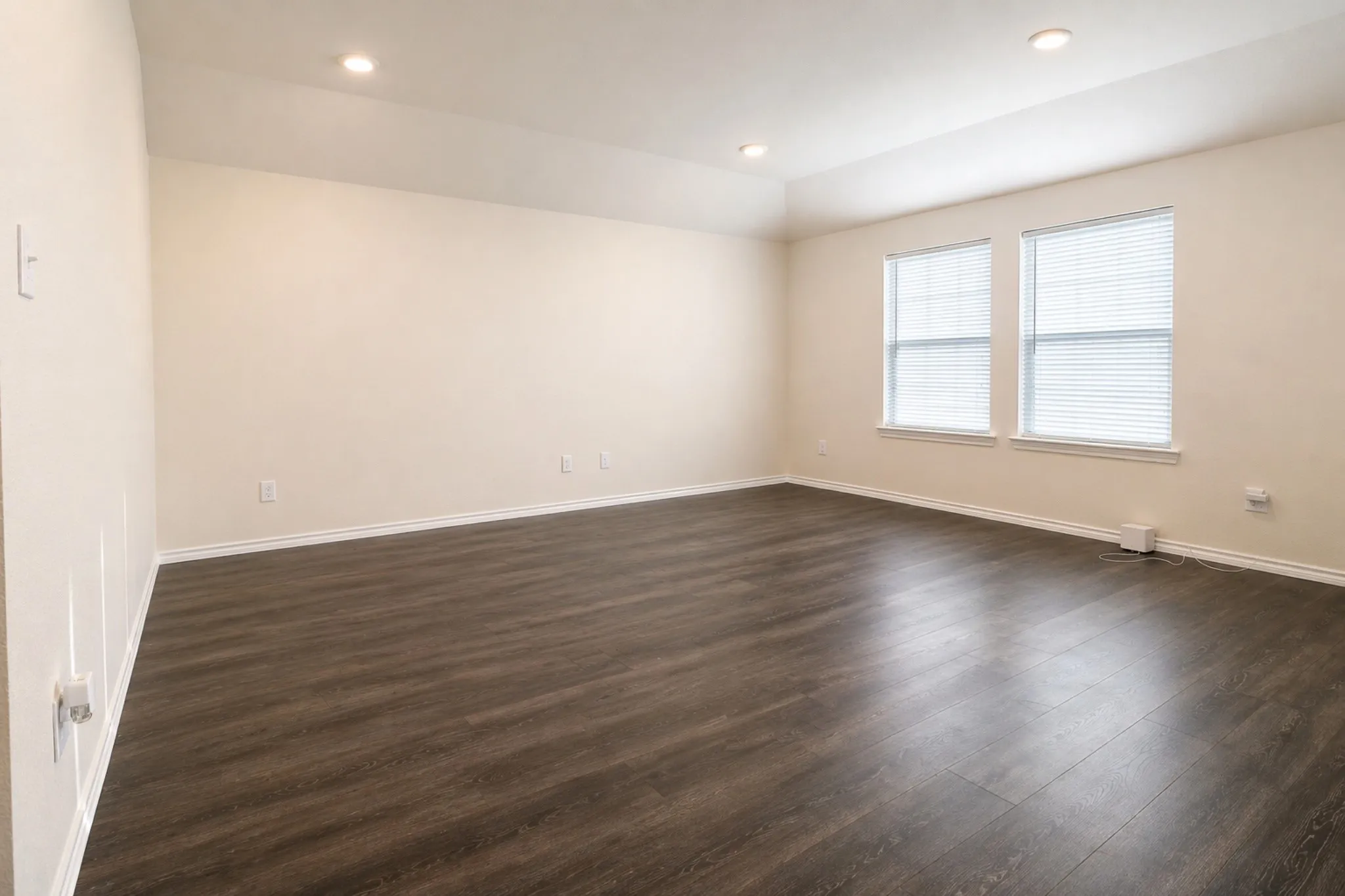 Spacious room featuring wood-finish flooring, recessed lighting, a tray ceiling, and two windows with blinds