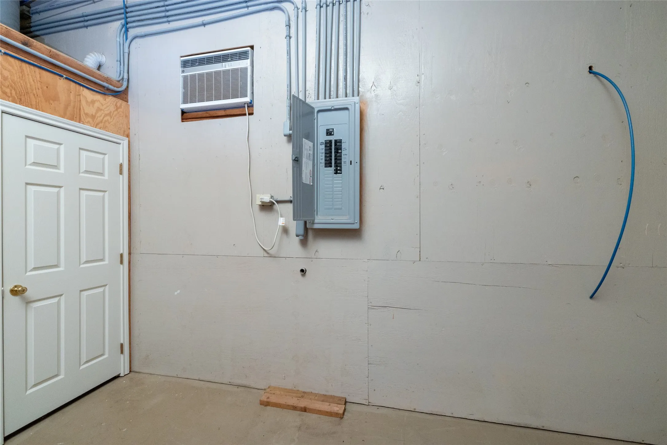 Utility space featuring exposed conduit, a central electrical panel, and a wall-mounted AC unit