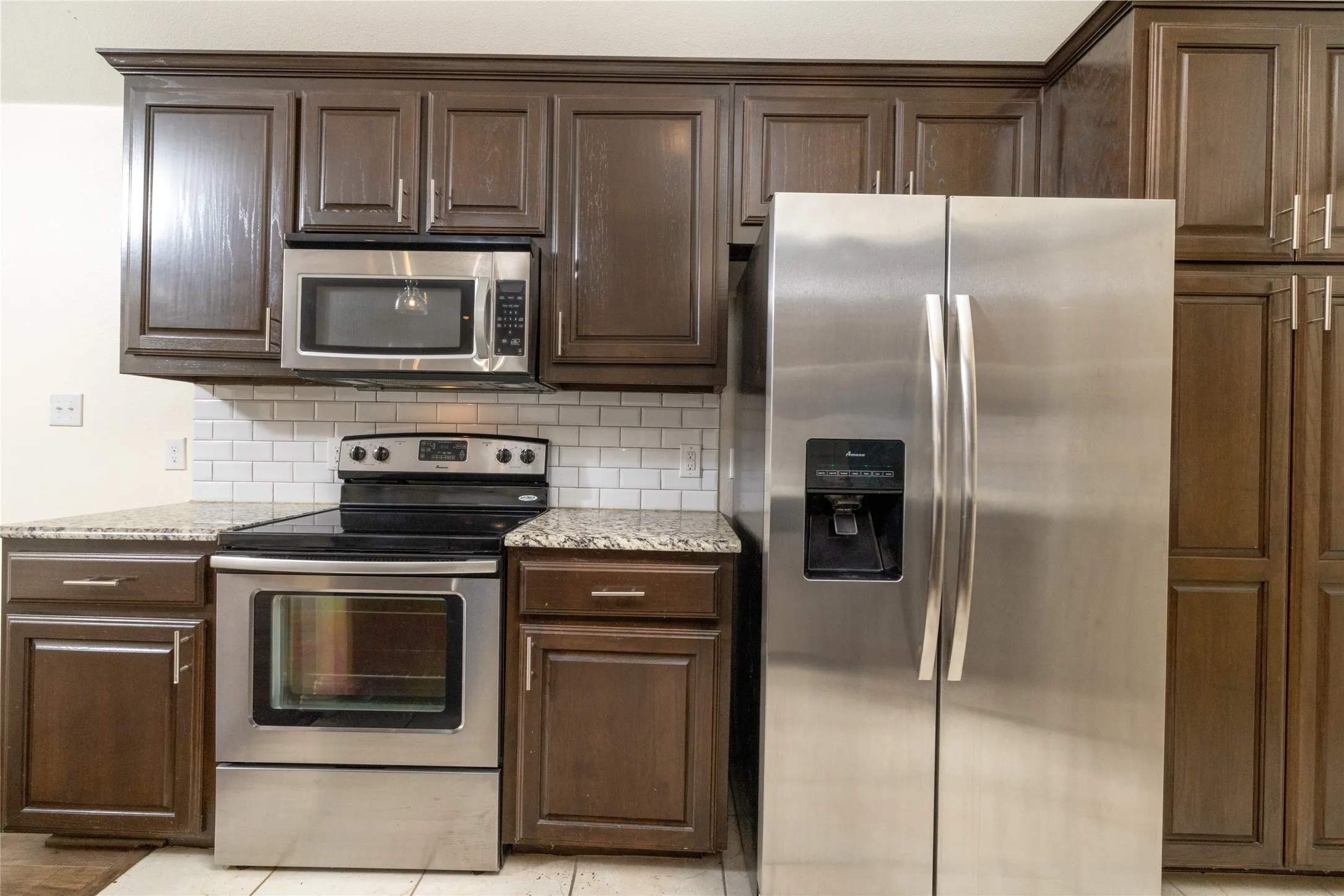 Kitchen featuring dark wood-finish cabinetry, stainless steel appliances, speckled stone countertops, and a subway tile backsplash