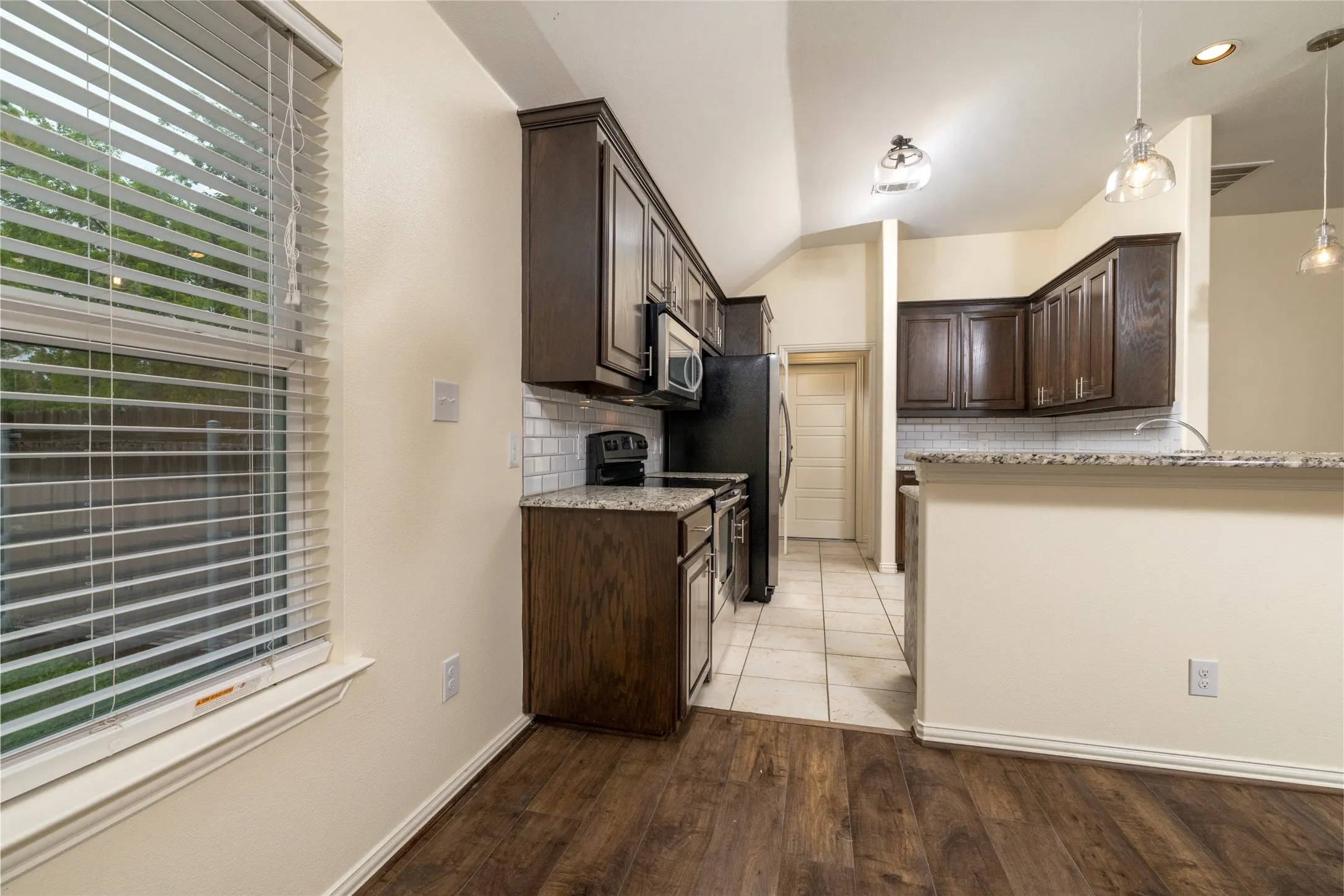 Kitchen featuring wood-finish flooring, dark wood cabinetry, and granite countertops