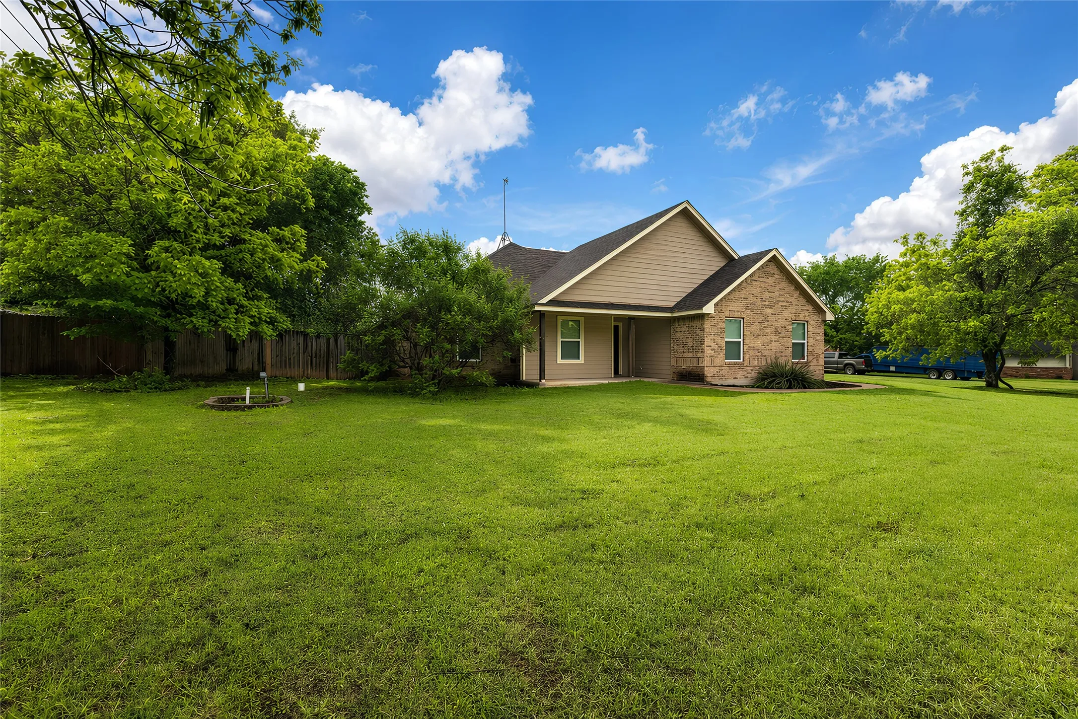 Expansive green lawn with a brown privacy fence and mature trees