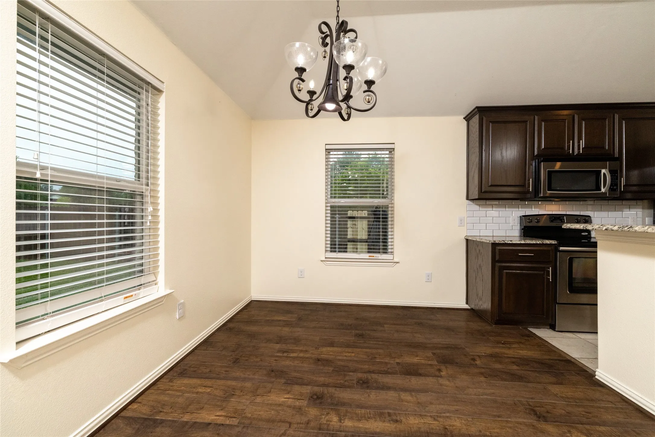 Open-concept dining space featuring wood-finish flooring, a decorative chandelier, and abundant natural illumination from multiple windows