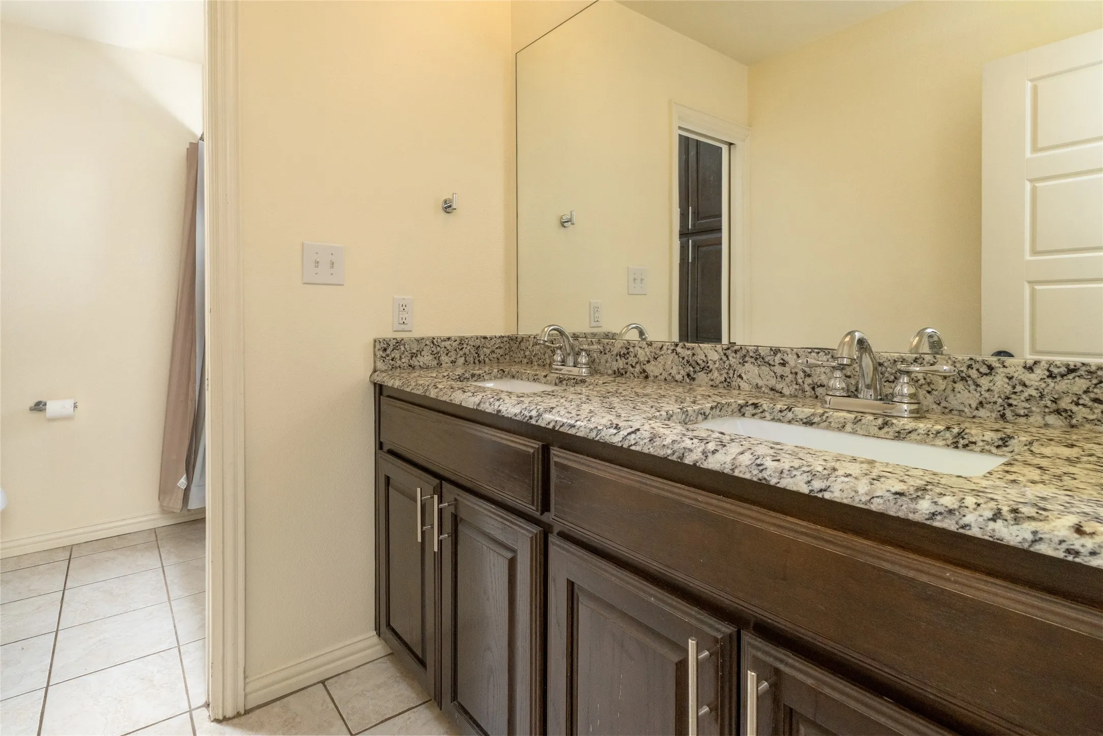 Dual vanity with granite countertop, integrated sinks, chrome fixtures, and dark wood cabinetry