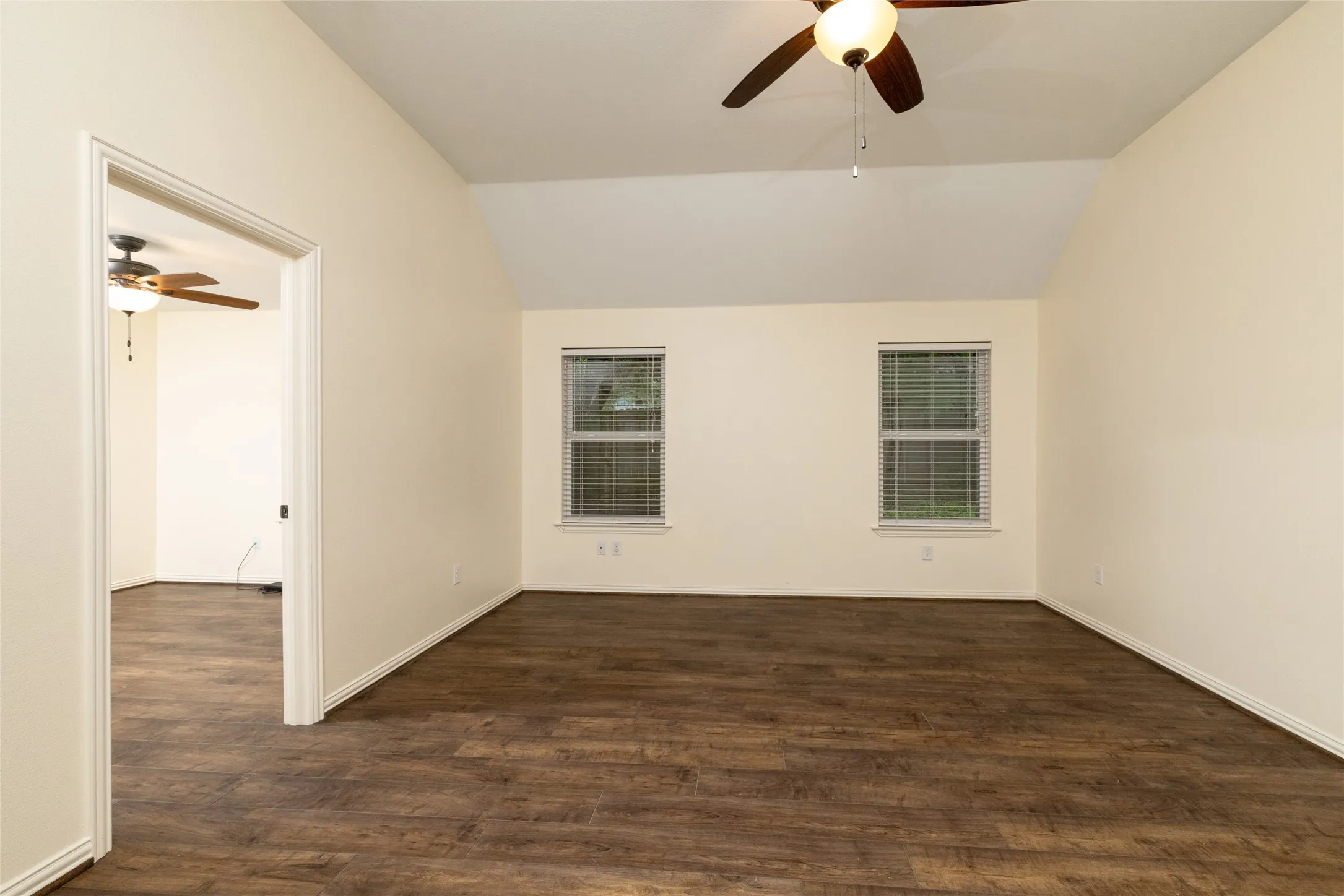 Spacious room featuring wood-finish flooring, vaulted ceilings, and two windows with blinds