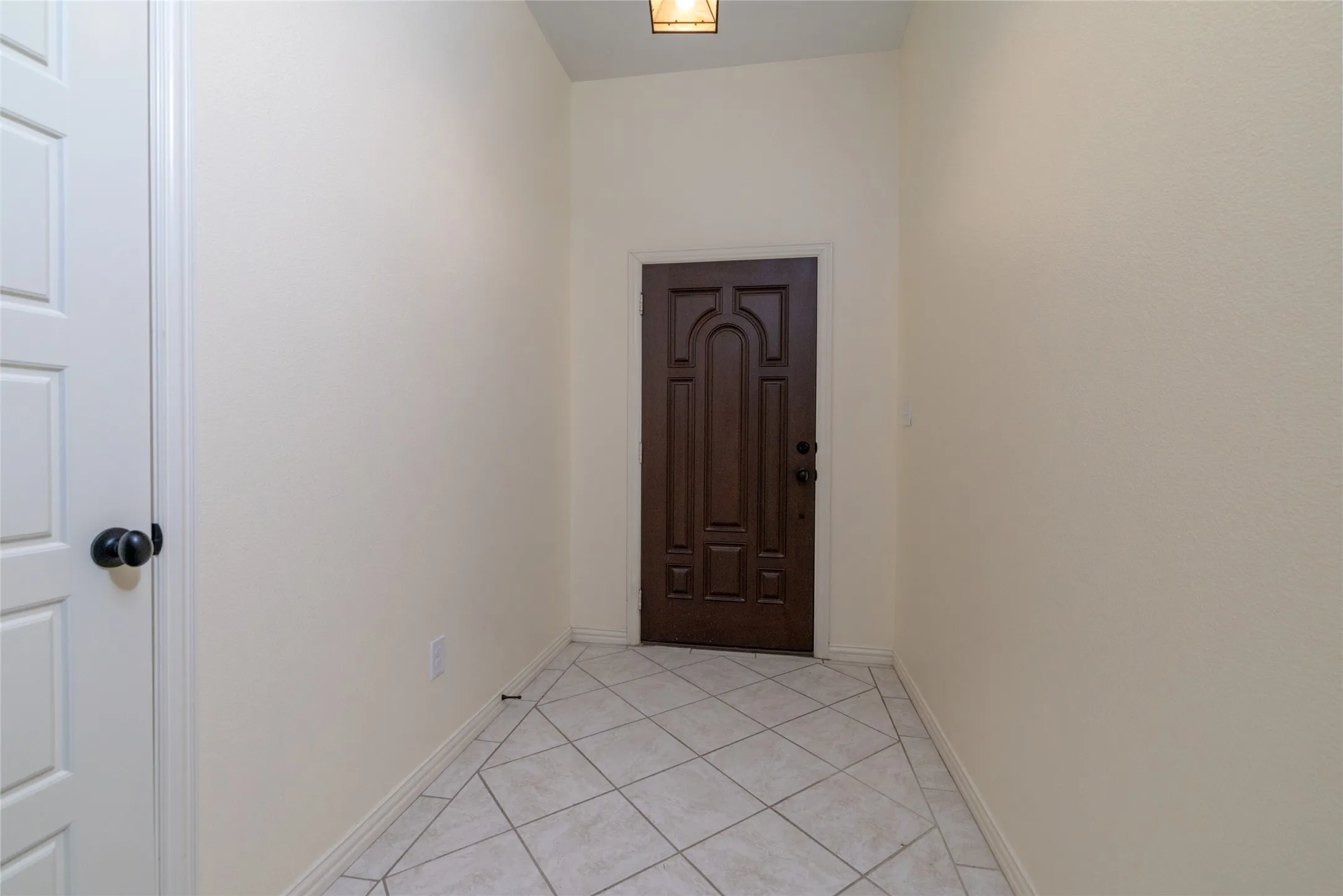 Entryway featuring a dark wood paneled door, light-toned textured walls, white trim, and a patterned tile floor