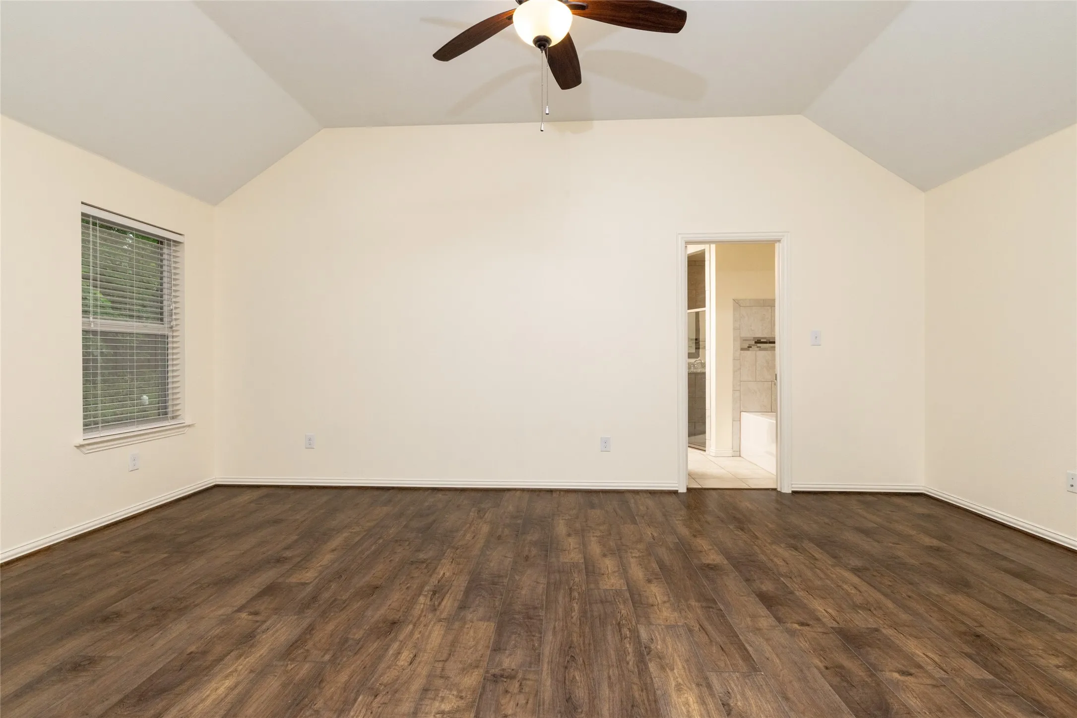 Spacious room featuring wood-finish flooring, vaulted ceilings, and a ceiling fan with light fixture