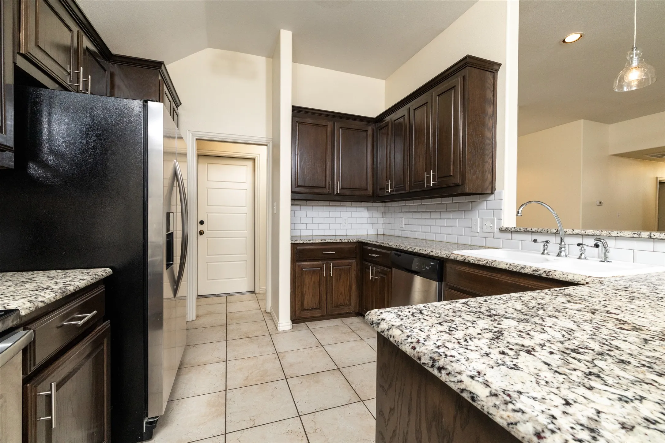Kitchen featuring dark wood cabinetry, light granite-finish countertops, and a white subway tile backsplash