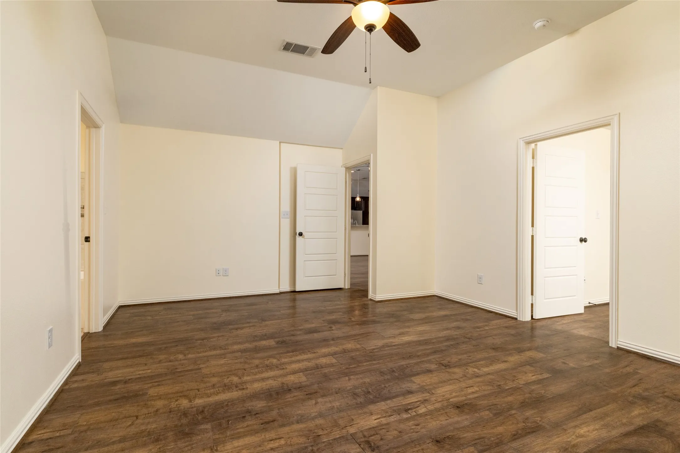 Spacious room featuring wood-finish flooring, vaulted ceilings, and a ceiling fan with light fixture
