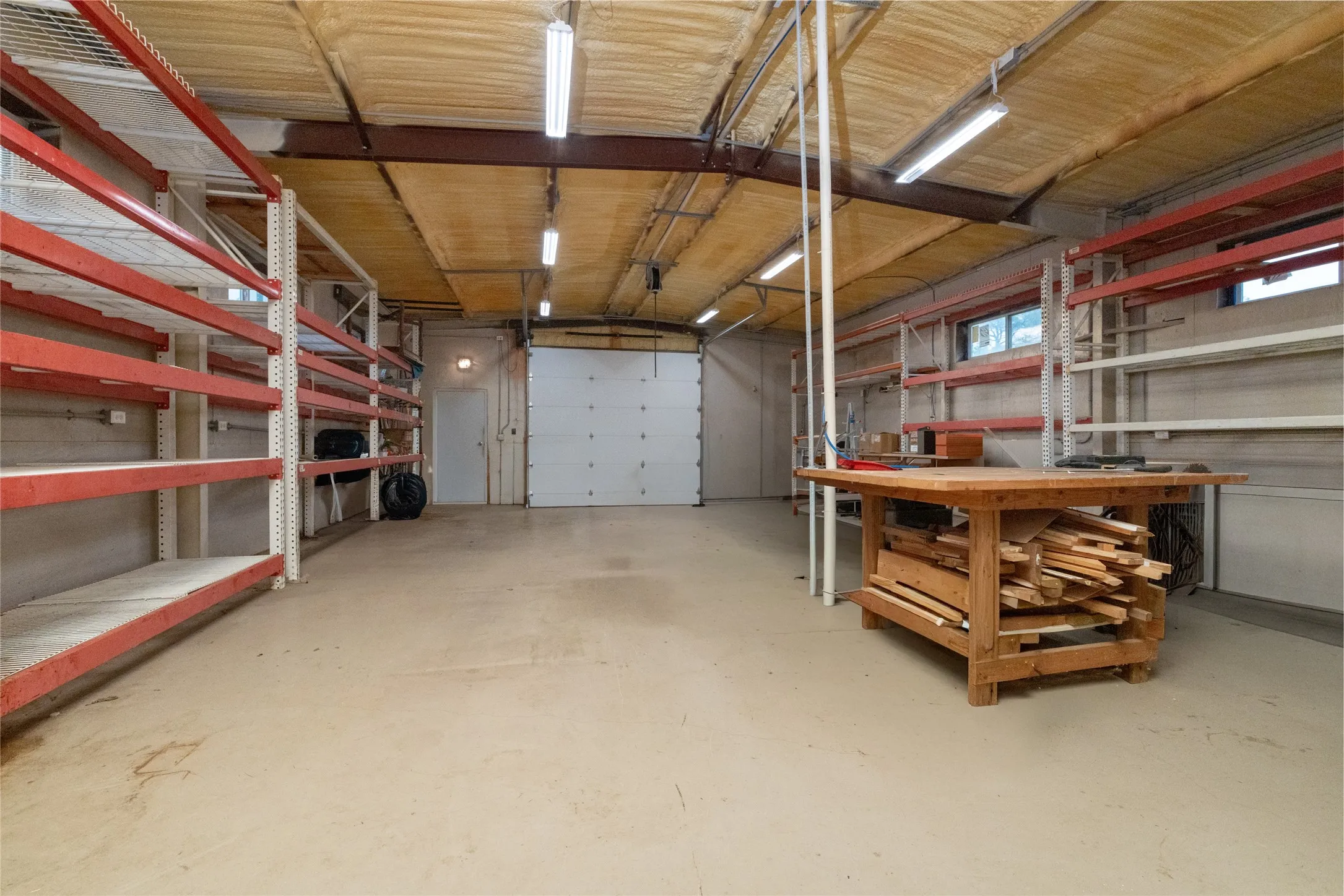 Spacious utility garage featuring a roll-up door, exposed metal beams, and a high ceiling with spray foam insulation