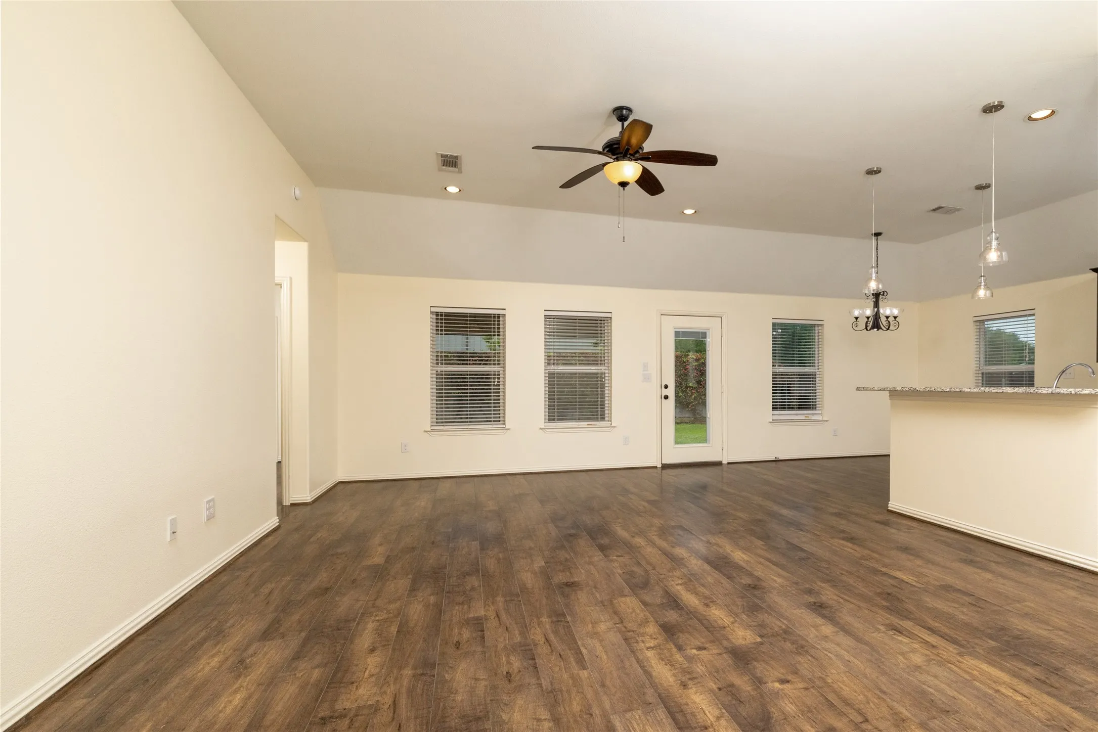 Spacious open-concept living area featuring wood-finish flooring, vaulted ceilings, and recessed lighting