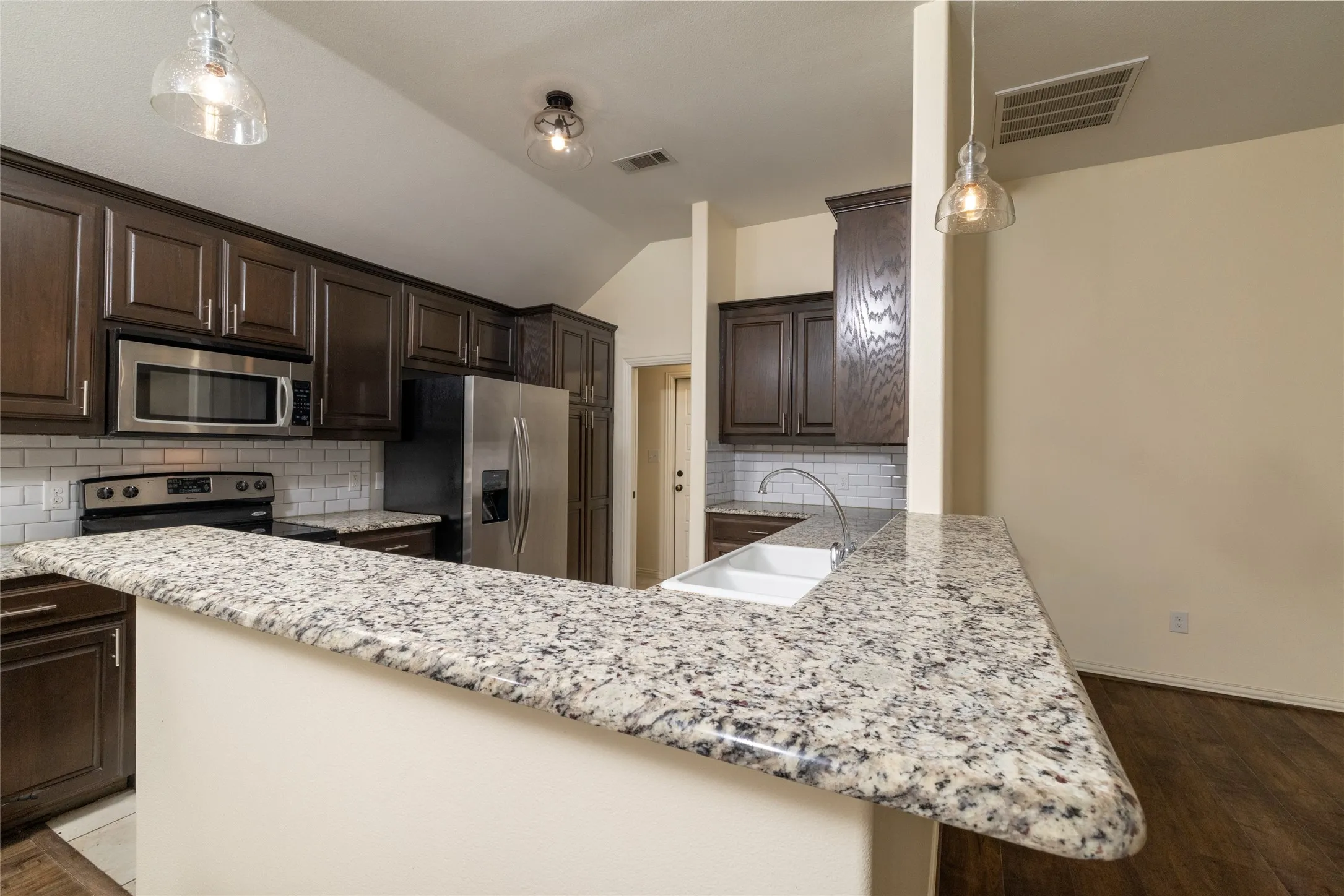 Kitchen featuring granite countertops, dark wood cabinetry, a white subway tile backsplash, stainless steel appliances, and wood-finish flooring