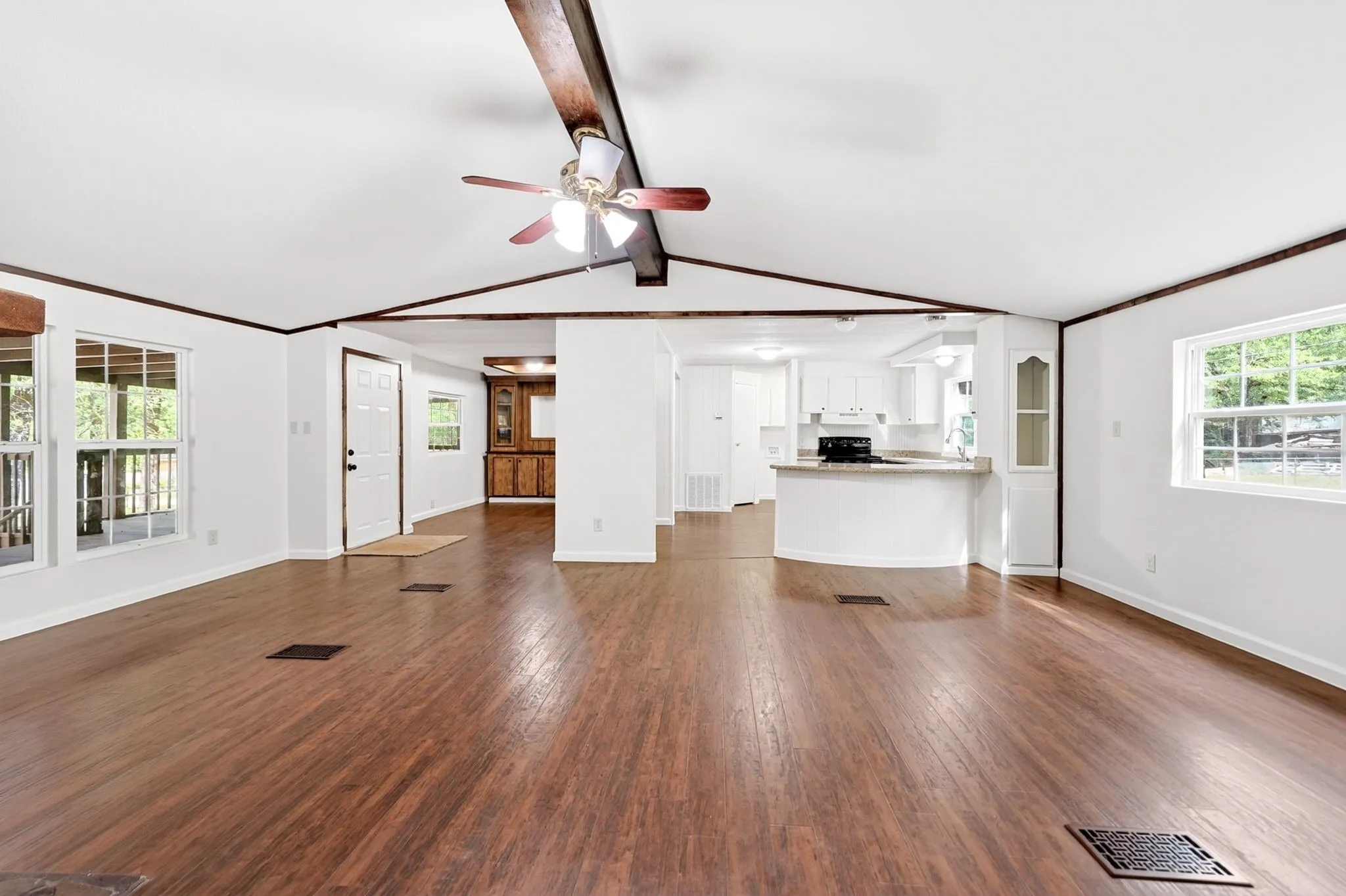 Spacious open-concept interior featuring wood-finish flooring, white walls, and exposed ceiling beams