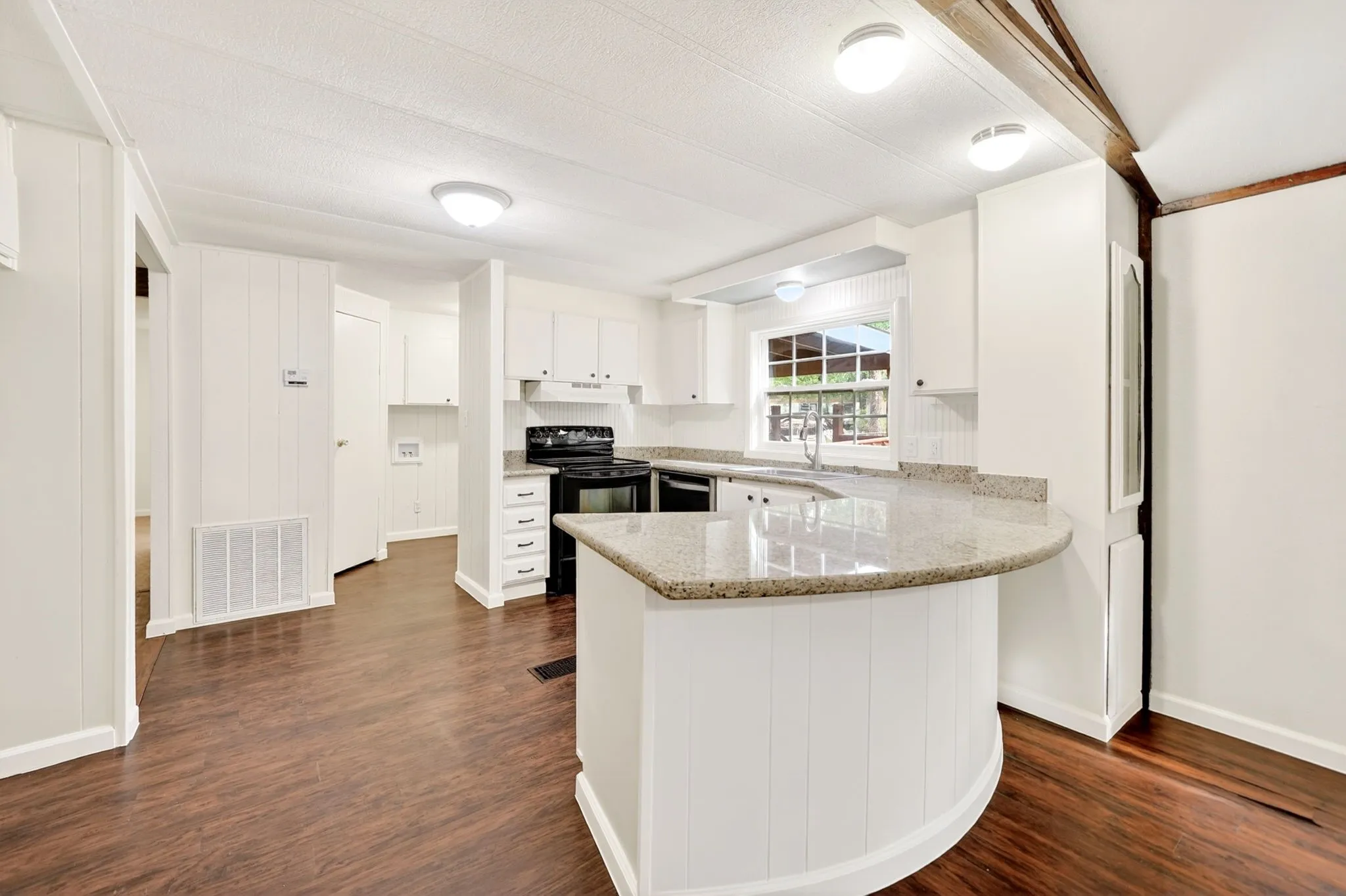 Kitchen featuring a curved breakfast bar with granite-style countertop, white cabinetry, dark wood-finish flooring, and black appliances