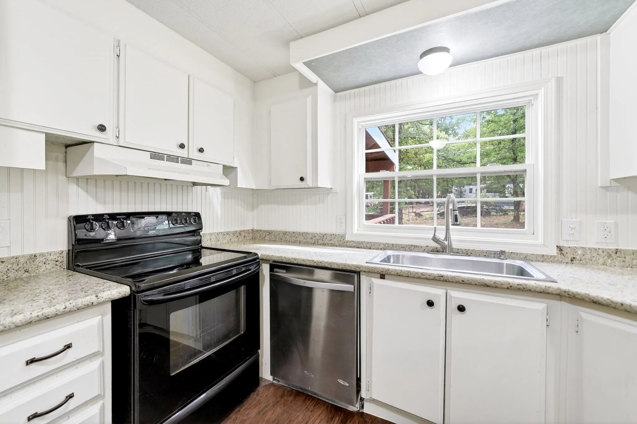 Kitchen featuring white cabinetry, granite-finish countertops, stainless steel sink with a high-arc faucet, and wood-finish flooring