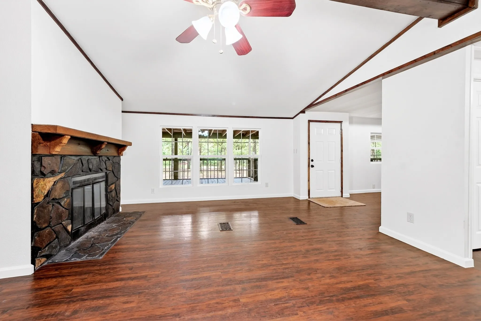 Spacious interior featuring wood-finish flooring, a stone fireplace with a wood mantle, a vaulted ceiling, and multiple windows