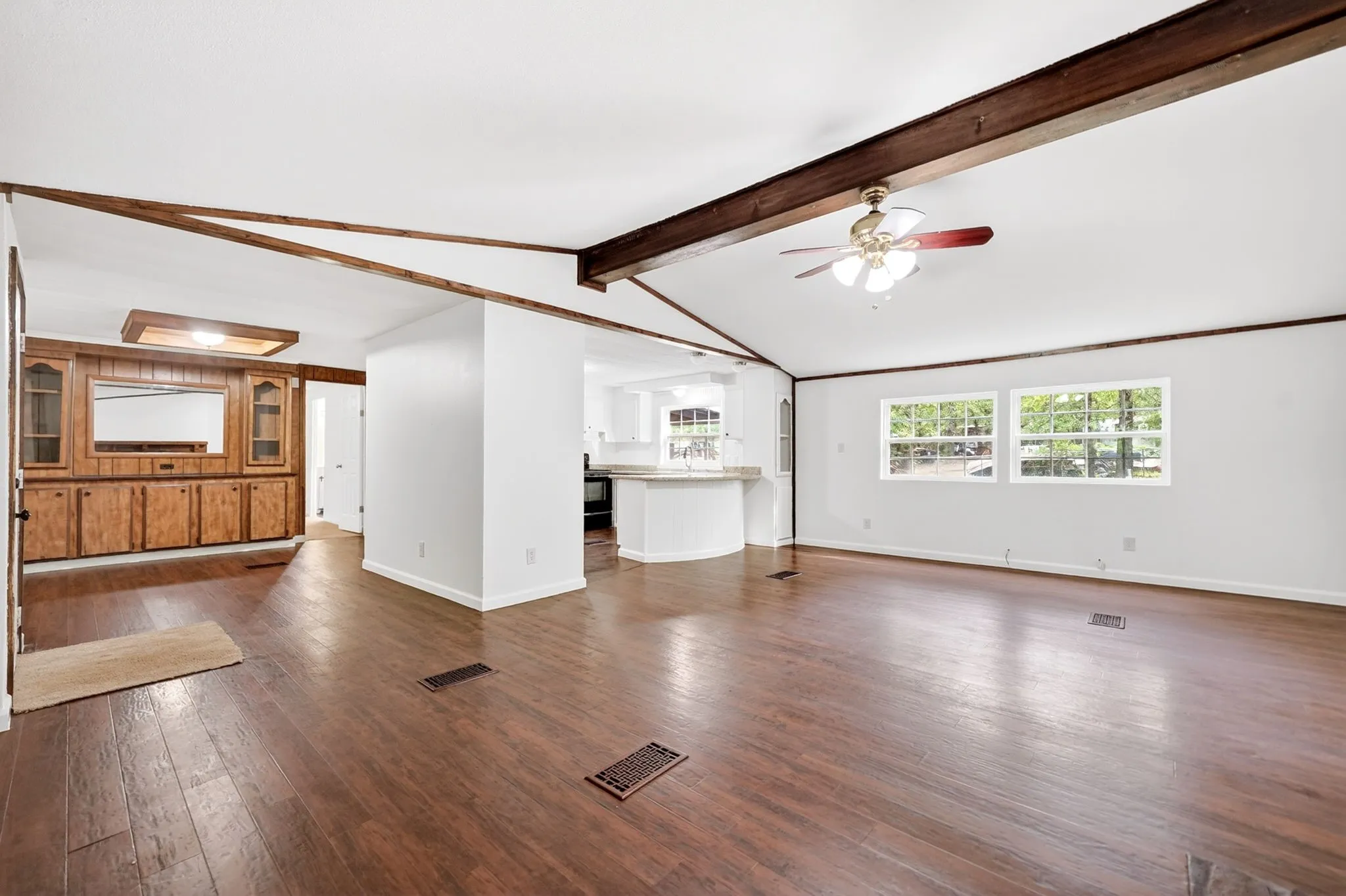 Spacious living area featuring wood-finish flooring, exposed ceiling beams, and a ceiling fan