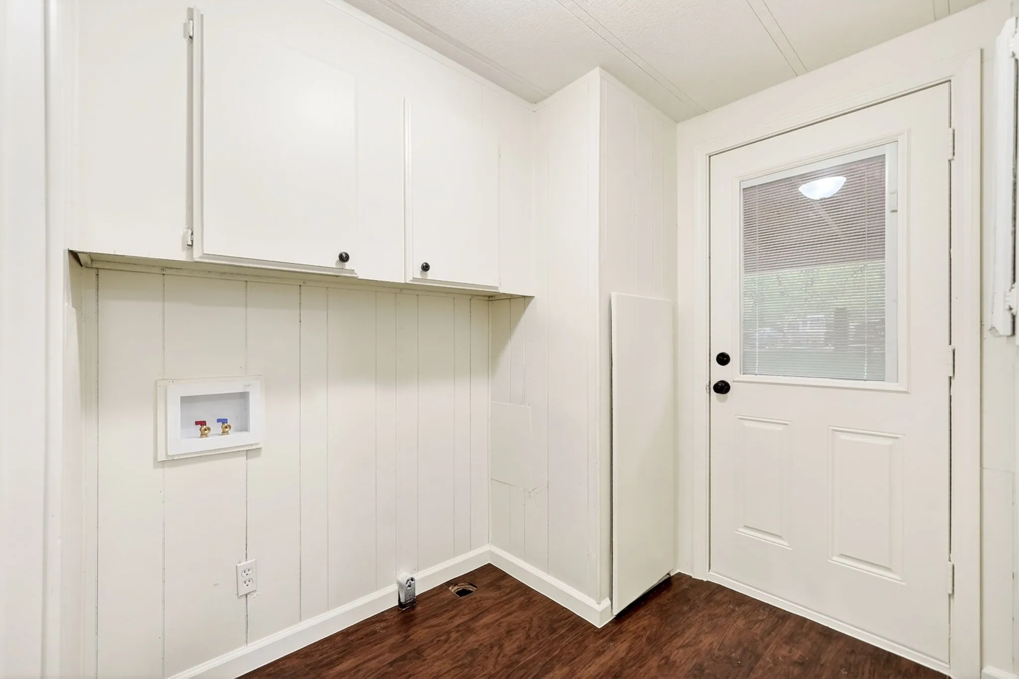 Utility space featuring wood-finish flooring, white paneled walls, and white cabinetry