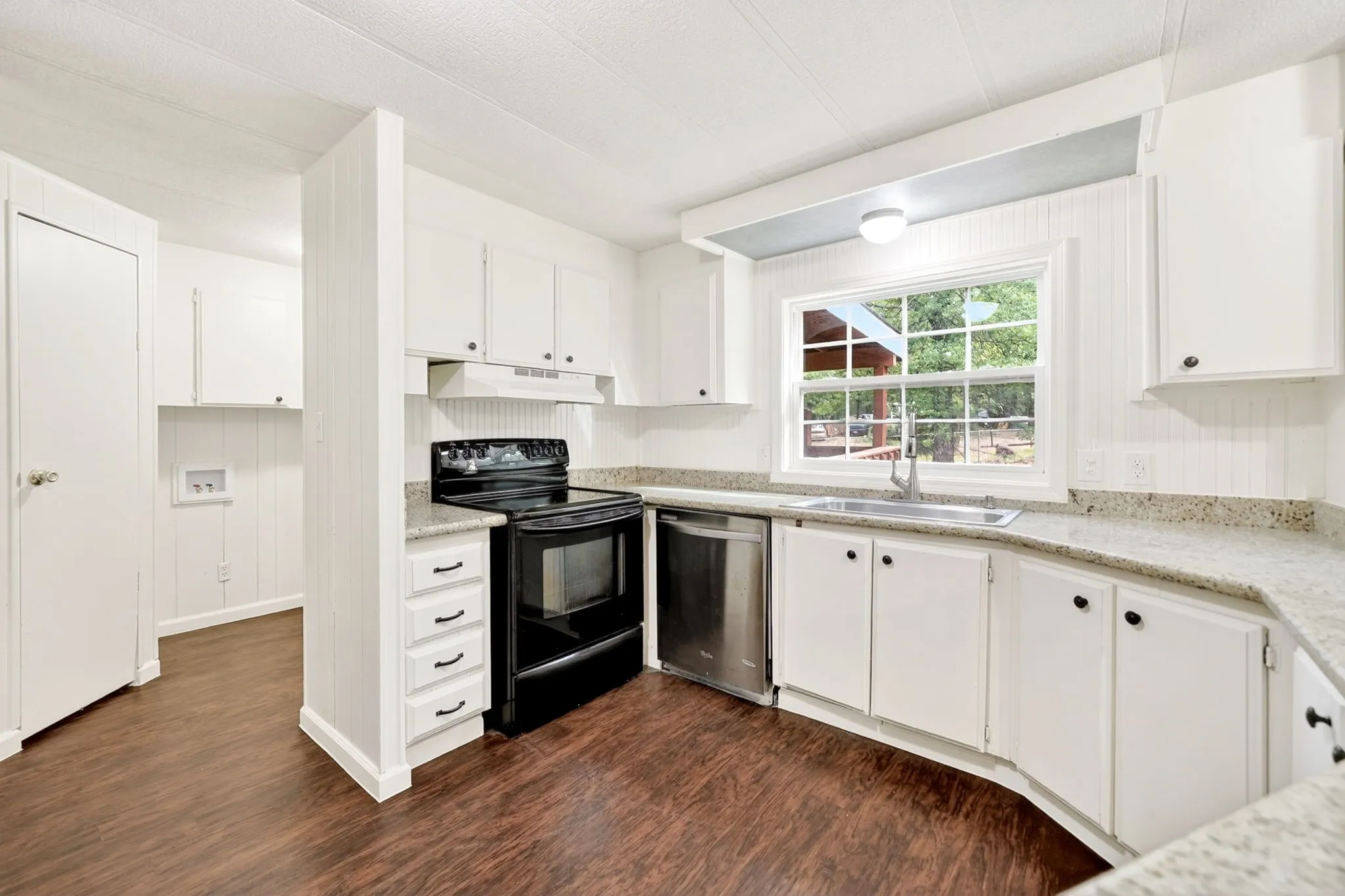 Kitchen featuring white cabinetry, light-toned countertops, dark wood-finish flooring, a stainless steel sink with a gooseneck faucet, and a black range