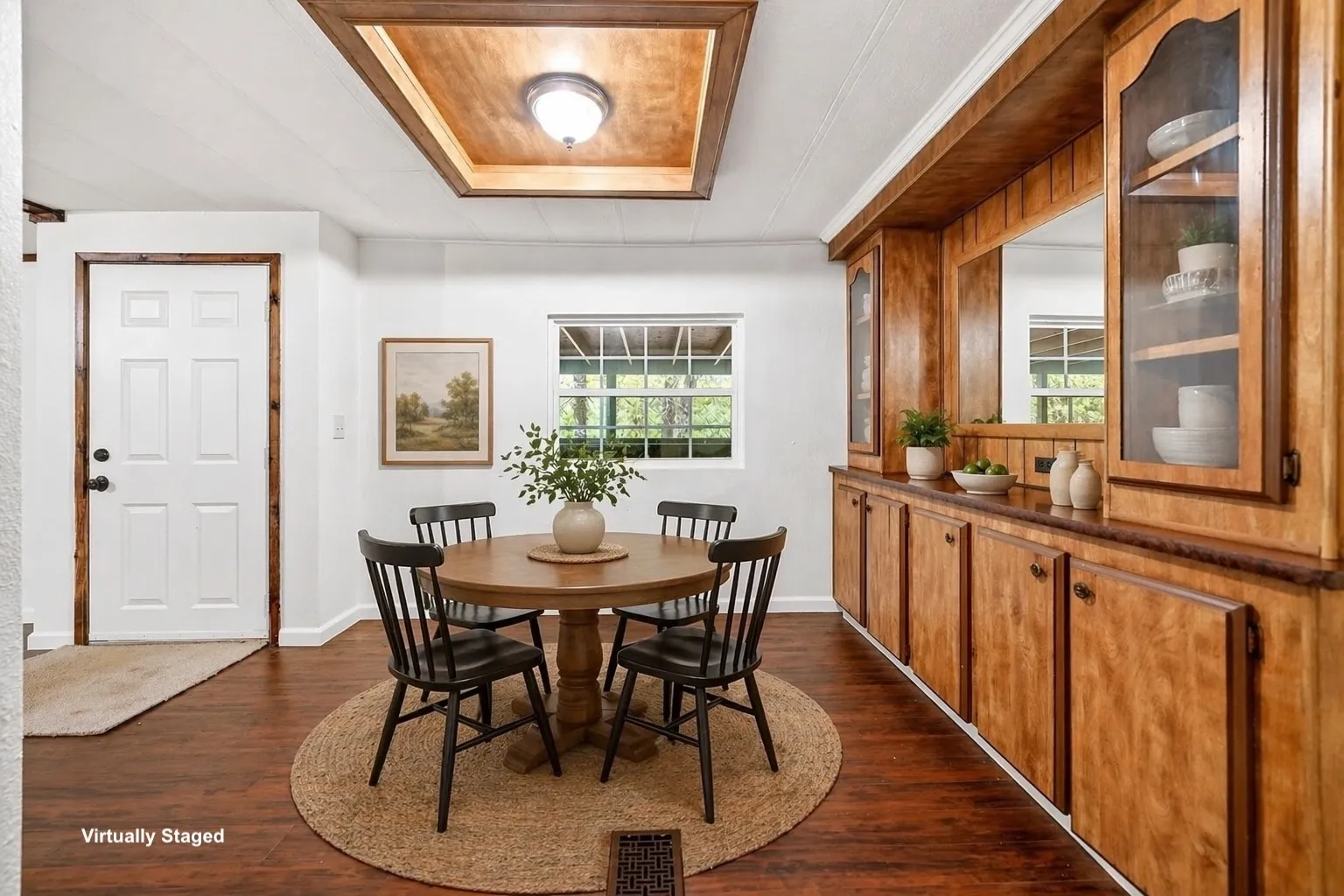 Dining area featuring expansive built-in wood cabinetry with glass-front display cabinets, wood-finish flooring, a recessed ceiling detail with wood paneling, and a large window providing natural light