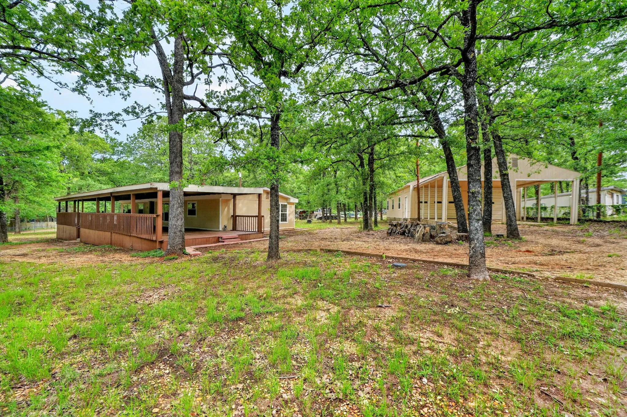 Expansive grounds featuring a light-toned structure with a full-length covered porch, a wooden ramp, and a separate covered carport area