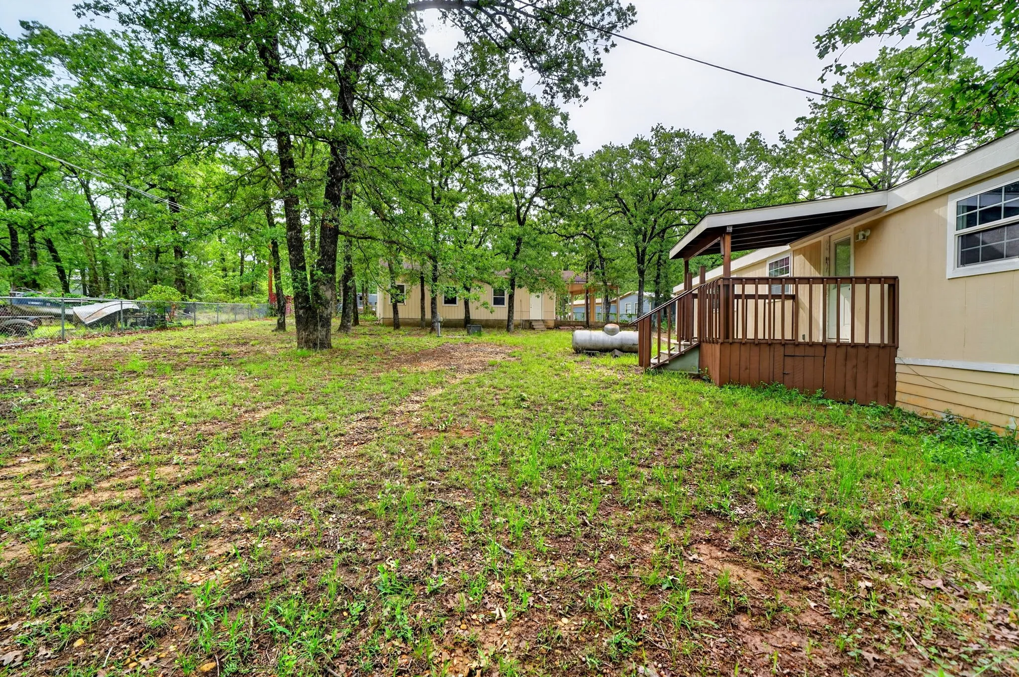 Expansive backyard featuring mature trees, a covered deck with wood railings, and a chain-link fence