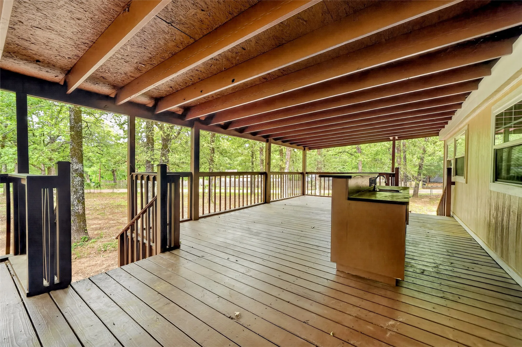 Expansive covered deck featuring wood-finish flooring, a built-in outdoor kitchen with a countertop and sink, and a wood railing system