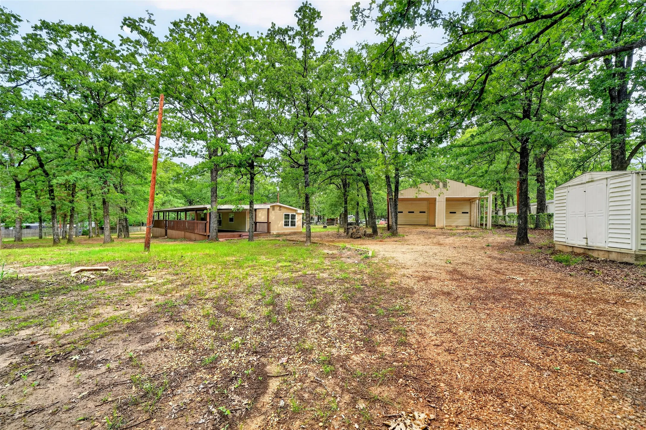 Wooded lot featuring a residential structure with an expansive covered porch, a separate two-bay garage, and a detached storage shed
