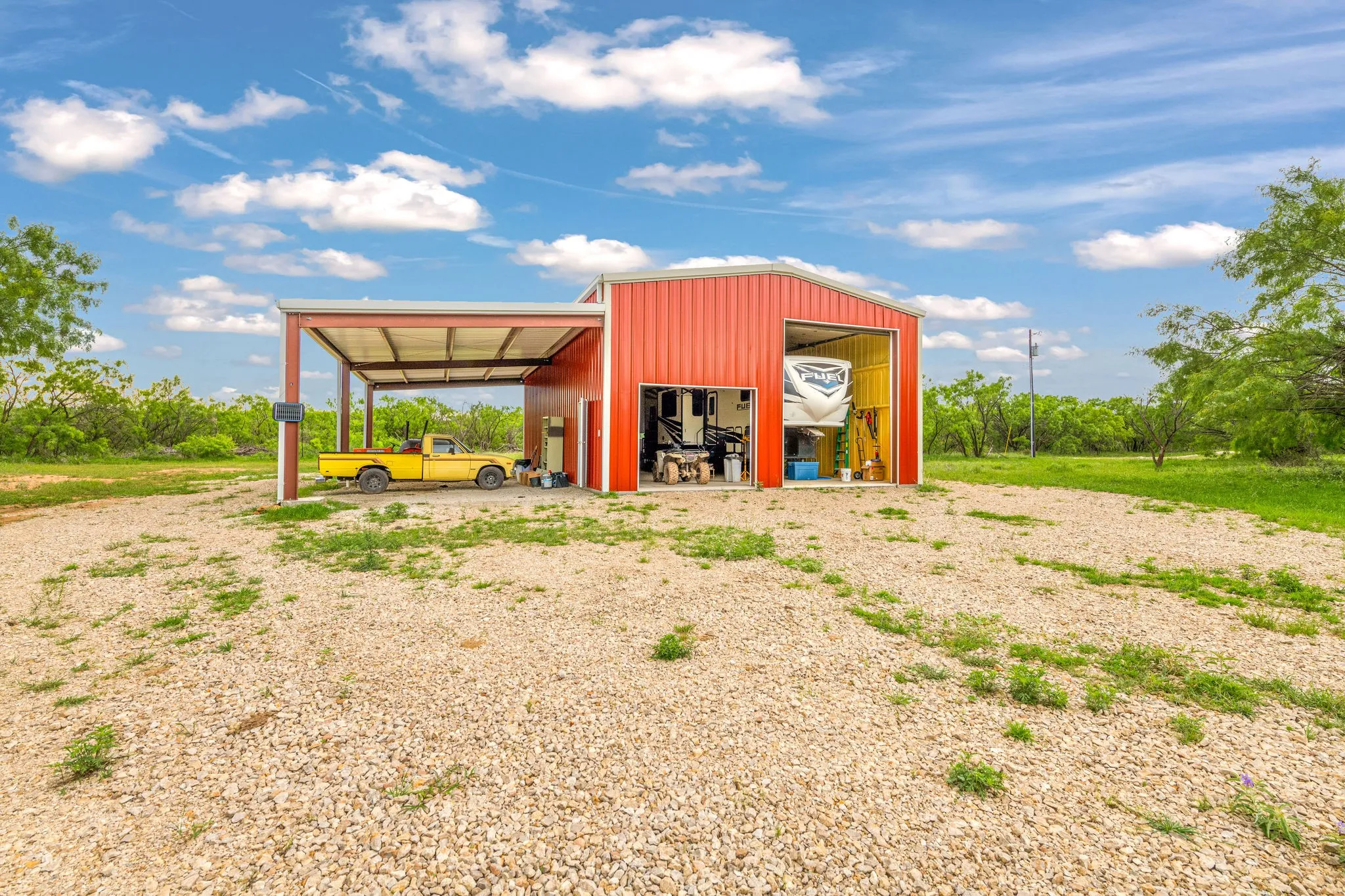 Red metal building featuring an attached covered lean-to, large bay door, and a smaller access door.