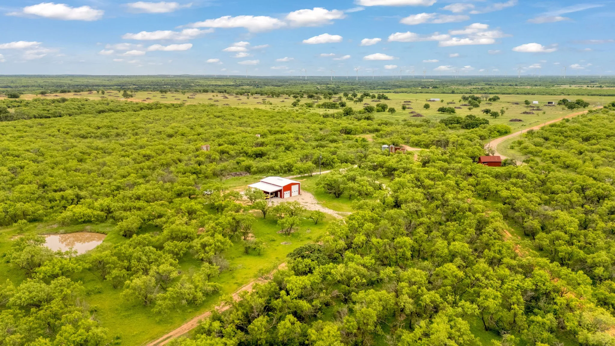 Expansive property featuring a red and white barn, a natural pond, and a winding unpaved road