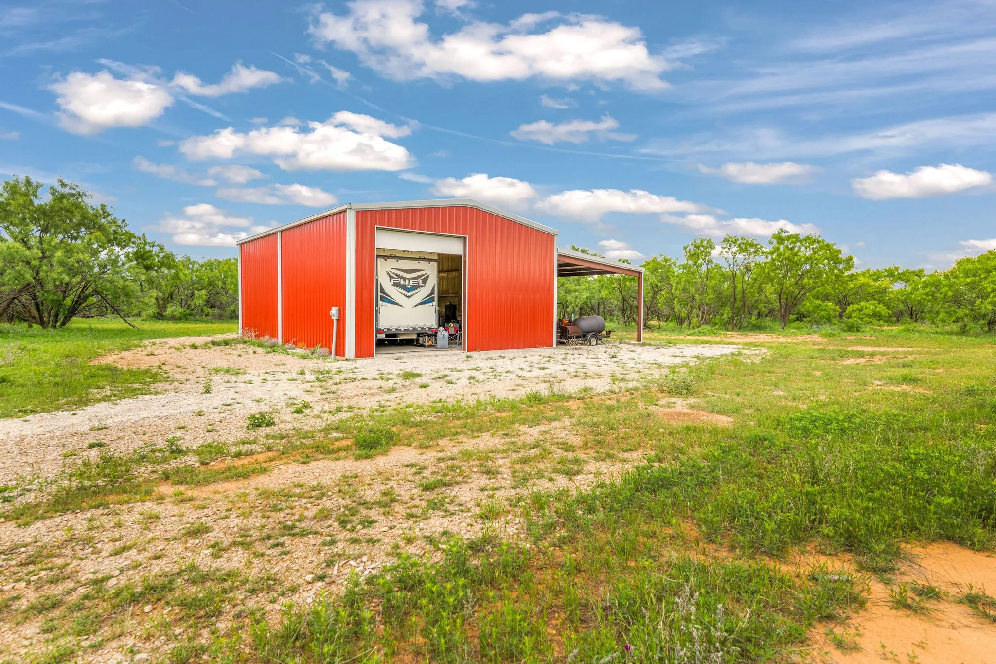 Red insulated metal building with 2 roll up doors for camper pull thru, an attached carport, gravel​​‌​​​​‌​​‌‌​‌‌​​​‌‌​‌​‌​‌​​​‌​​ pad.