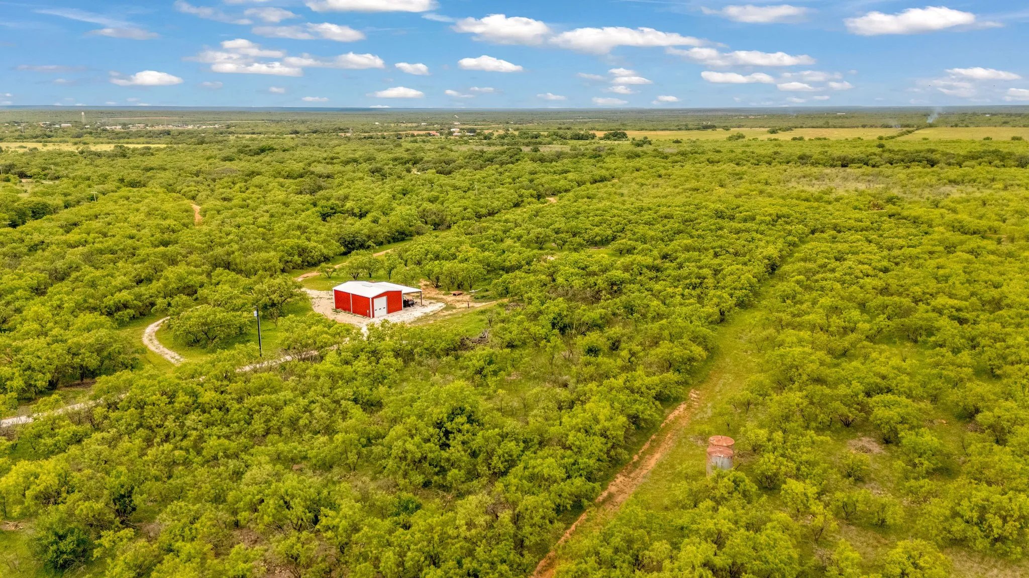 Extensive acreage featuring dense, mature tree cover, a red metal building with a white roof, and a winding dirt path