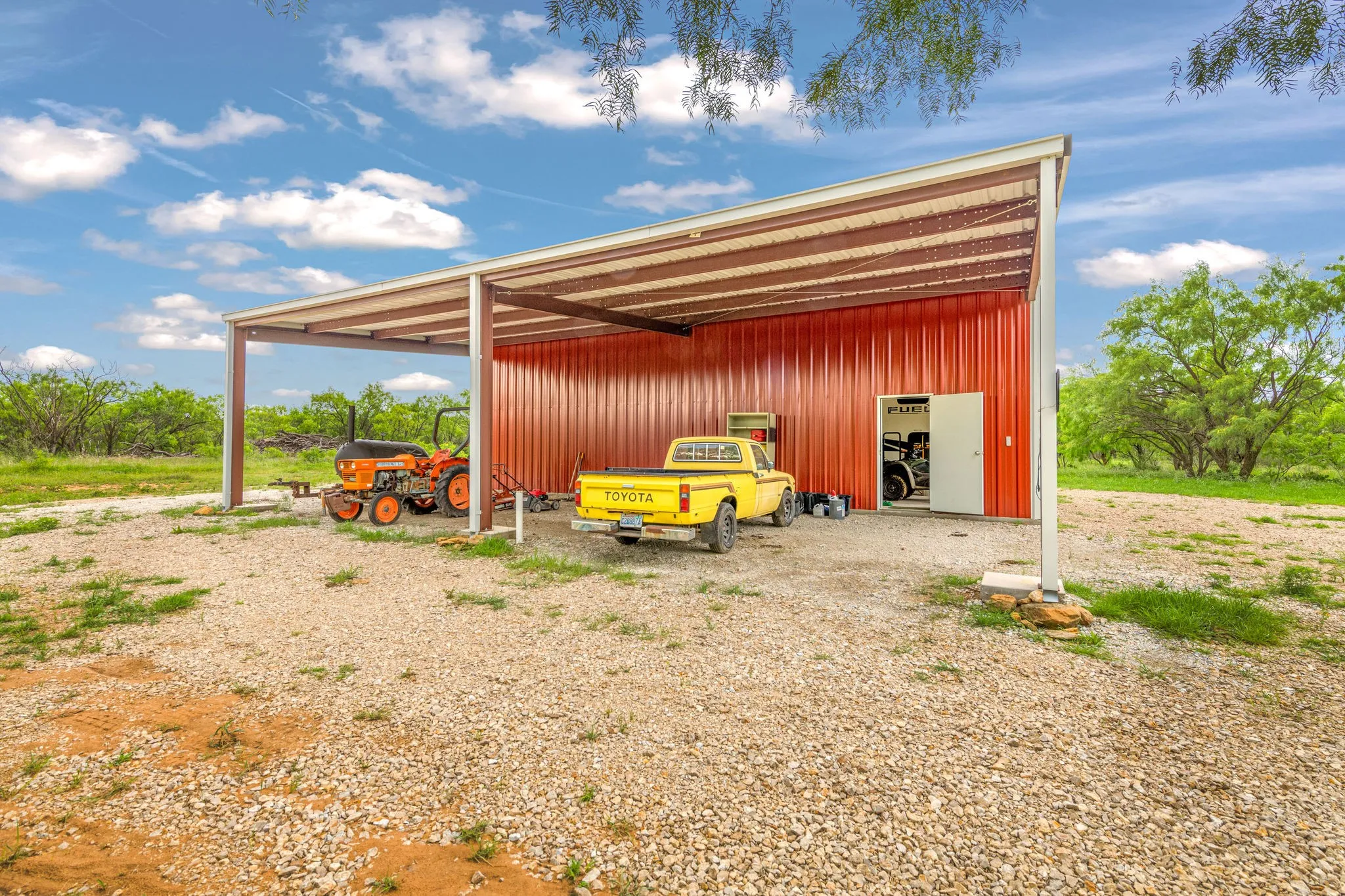 Metal storage building with a red corrugated exterior, featuring an attached open-sided carport with gutters.
