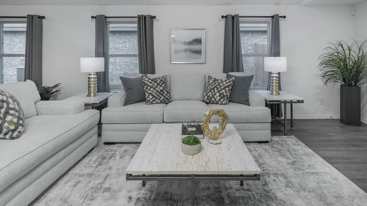 Spacious living area featuring light-toned walls, multiple windows with dark drapery, and wood-finish flooring