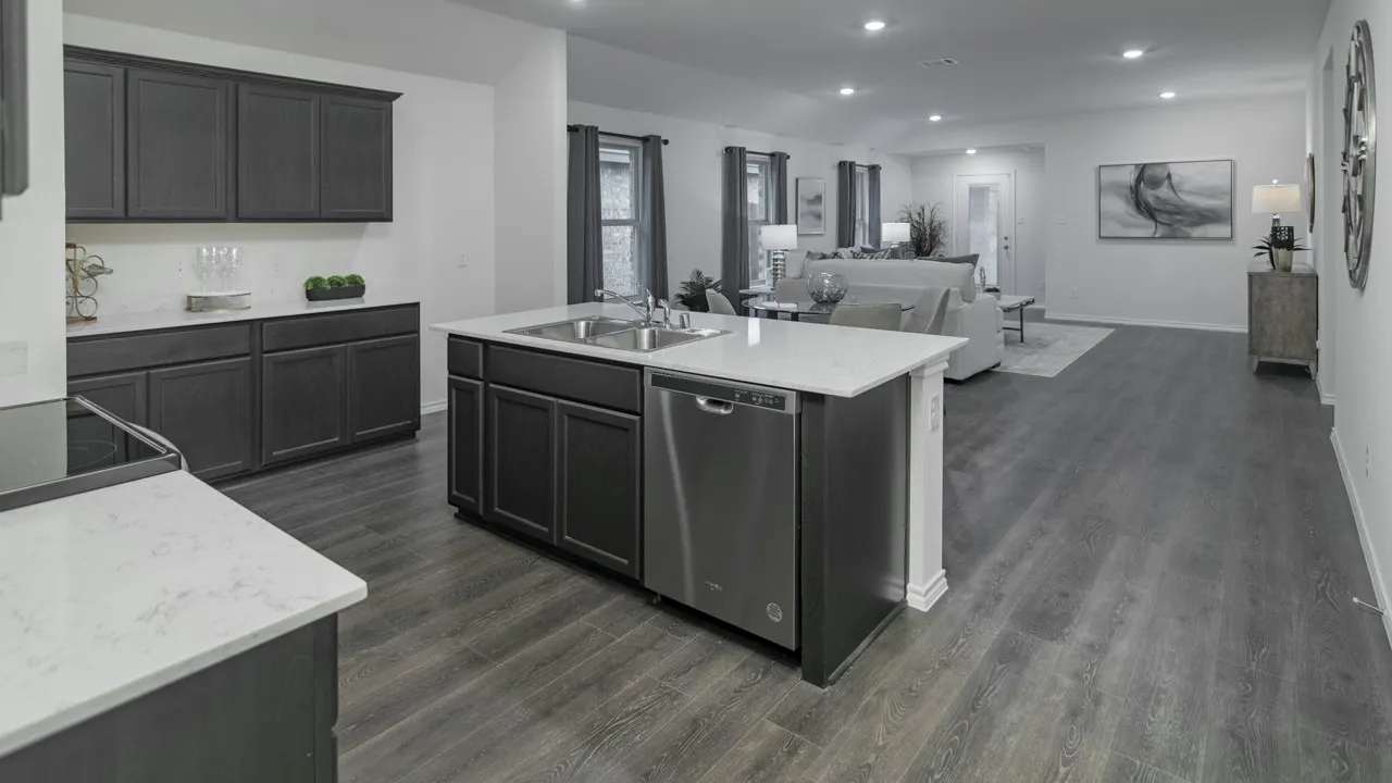 Open-concept kitchen featuring dark cabinetry, white countertops, stainless steel appliances, a kitchen island with an undermount sink, and wood-finish flooring