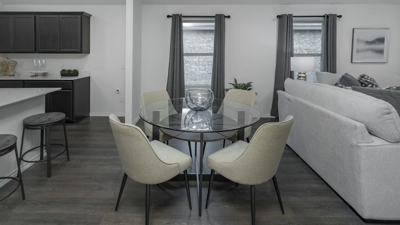 Open-concept interior featuring wood-finish flooring, a kitchen with dark cabinetry and light countertops, and a dining area with a glass-top table