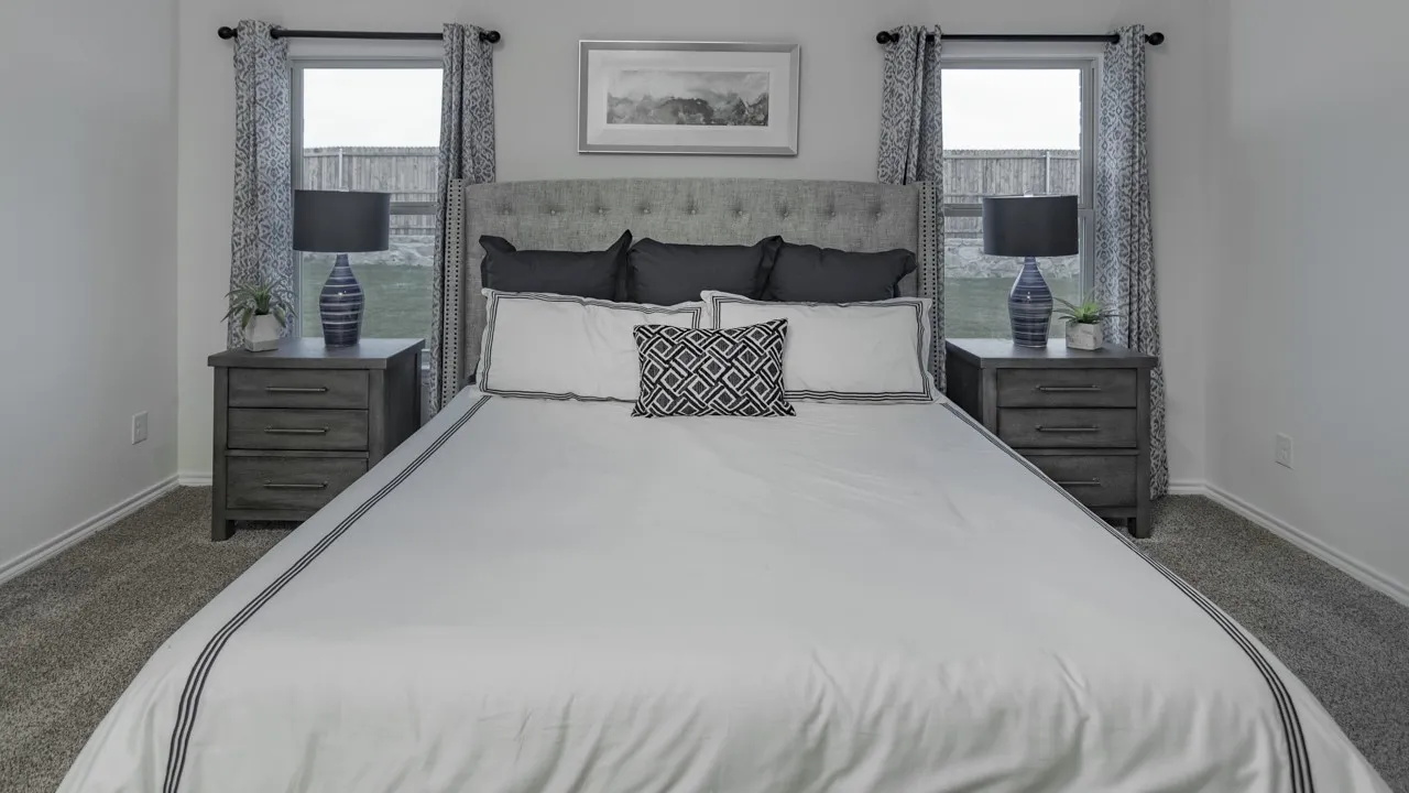 Spacious sleeping area featuring a tufted fabric headboard, dual windows with curtains, and plush carpeting