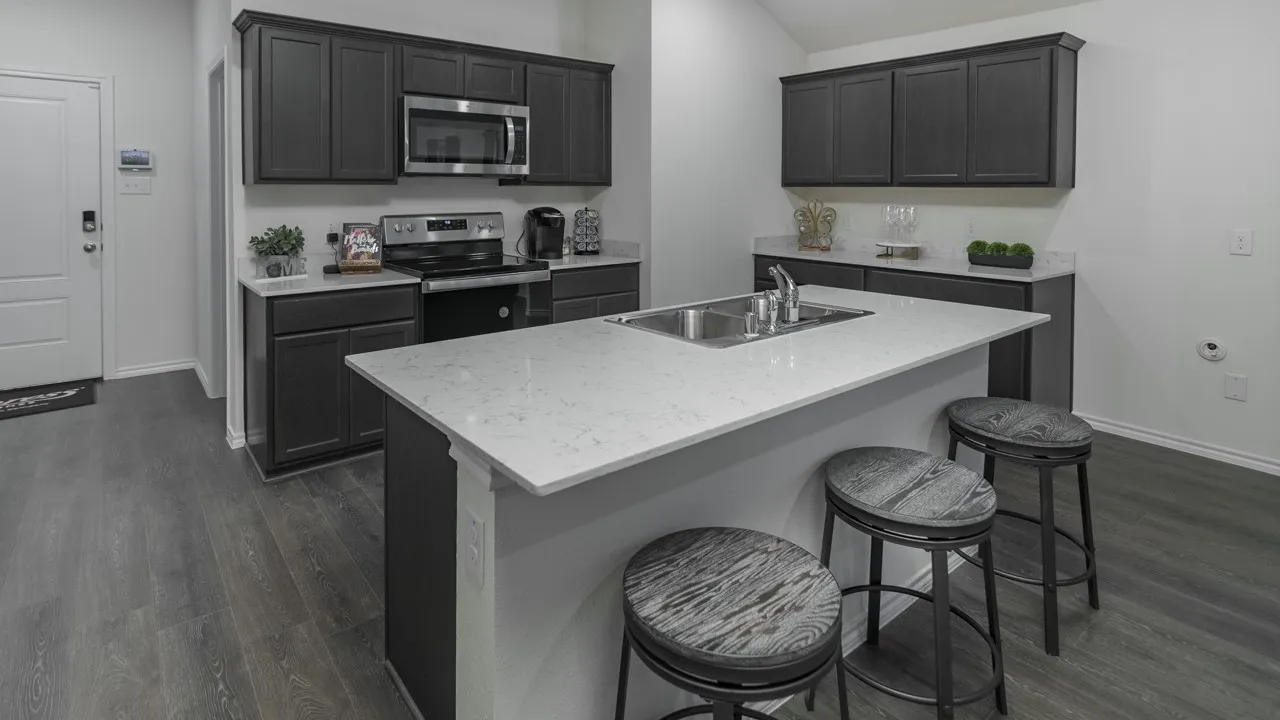 Contemporary kitchen featuring a center island with an undermount sink, dark wood-finish cabinetry, light-toned countertops, stainless steel appliances, and wood-finish flooring