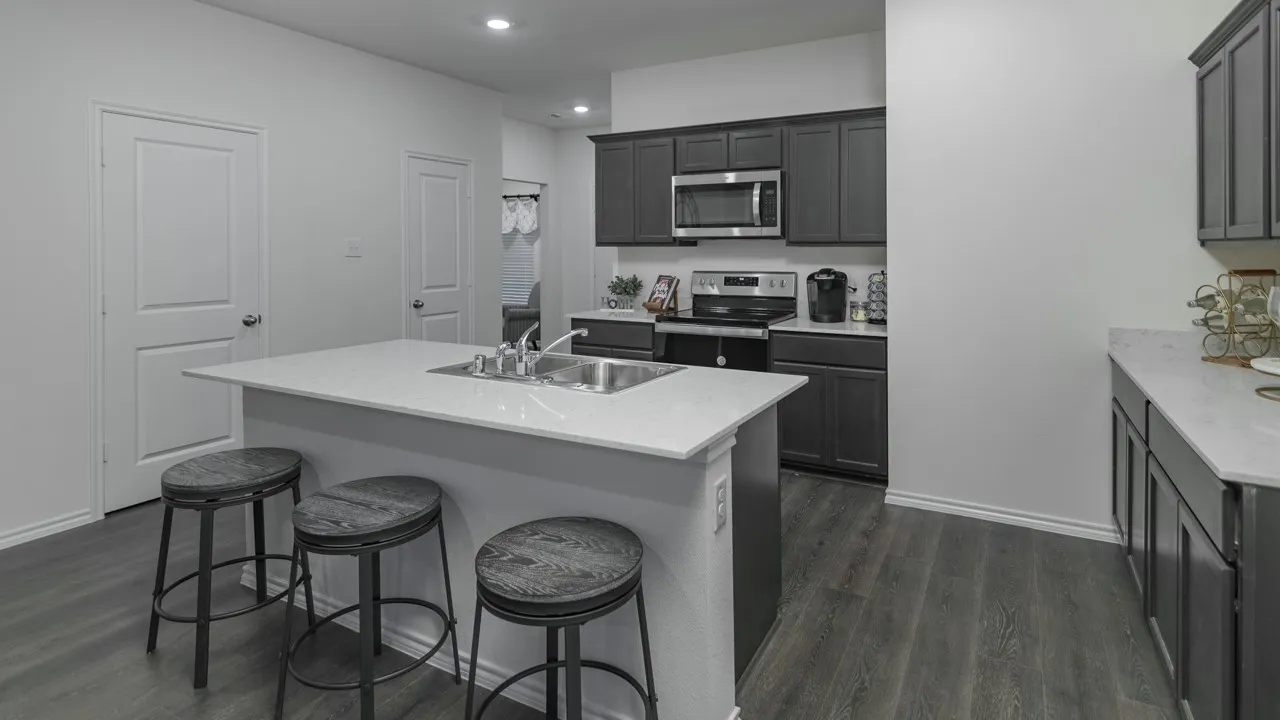 Bright kitchen featuring a central island with an undermount double basin sink, light-toned countertops, dark cabinetry, and wood-finish flooring
