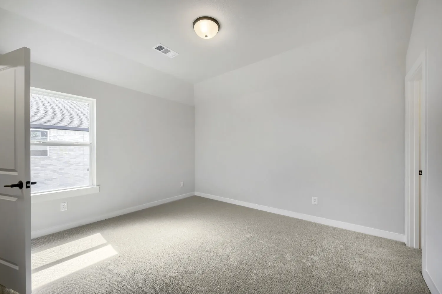 This room features light gray wall paint, a single window with white trim, a flush mount ceiling light, and gray carpeting