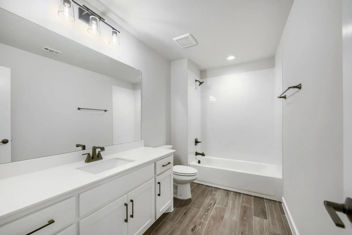 Bathroom featuring a white vanity with integrated sink, white cabinetry, dark bronze hardware, and wood-finish flooring
