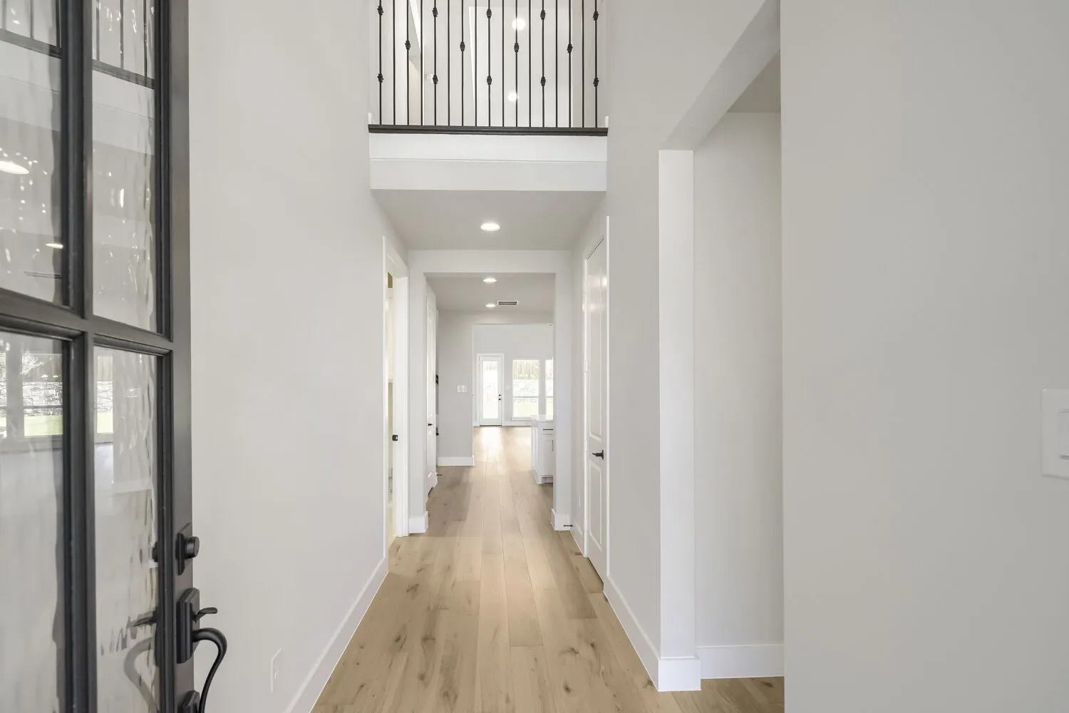 Foyer featuring a two-story ceiling, wood-finish flooring, a contemporary iron and glass entry door, recessed lighting, and a second-story overlook with an iron balustrade