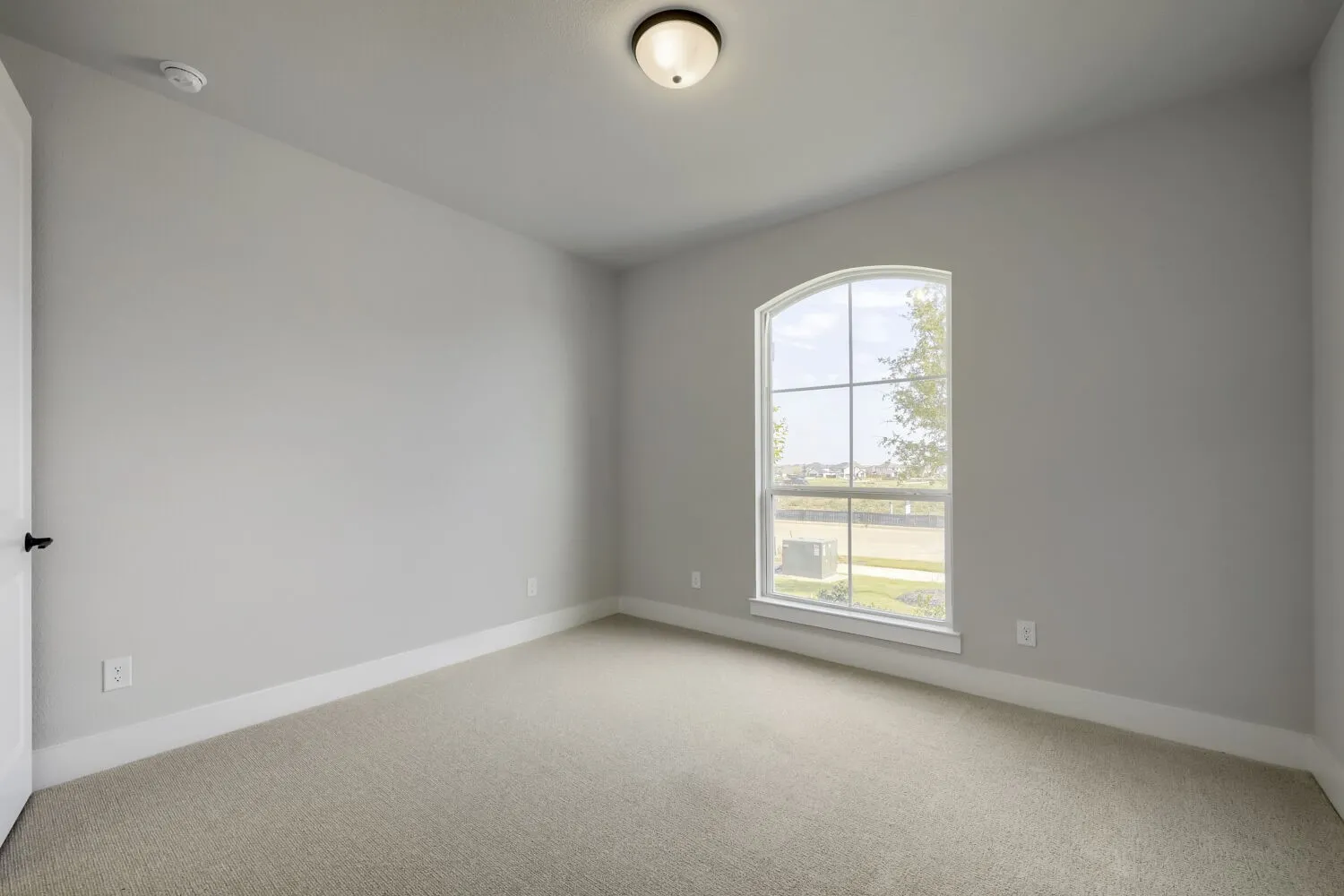 Room featuring a large arched window with grid-patterned panes, light gray wall tones, neutral carpeting, and white baseboards