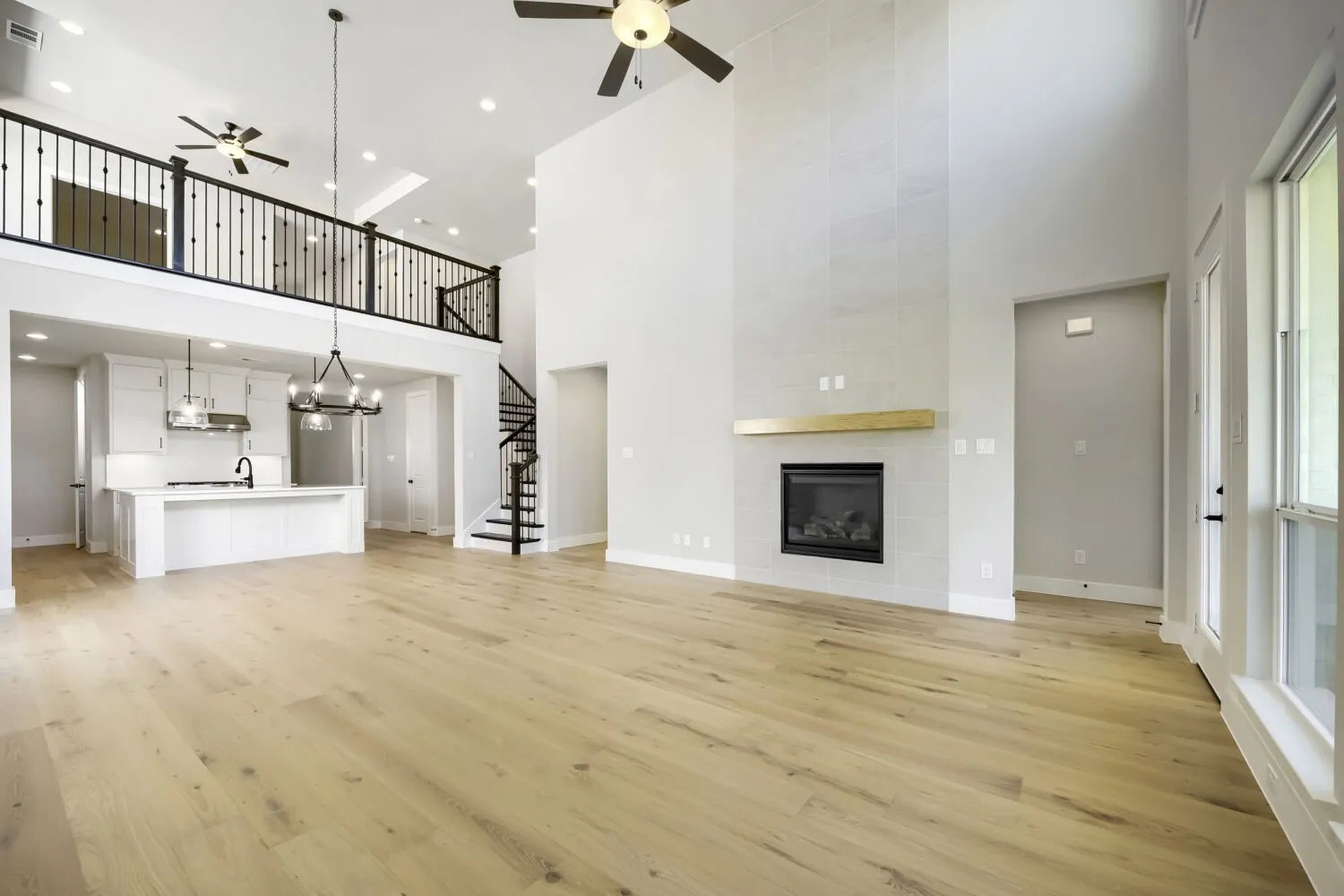 Spacious living area featuring high ceilings, wood-finish flooring, and a modern fireplace with a light wood mantel