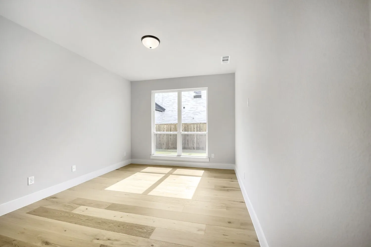 Room featuring a large window, light wood-finish flooring, white baseboards, light neutral wall paint, and a flush-mount ceiling light fixture