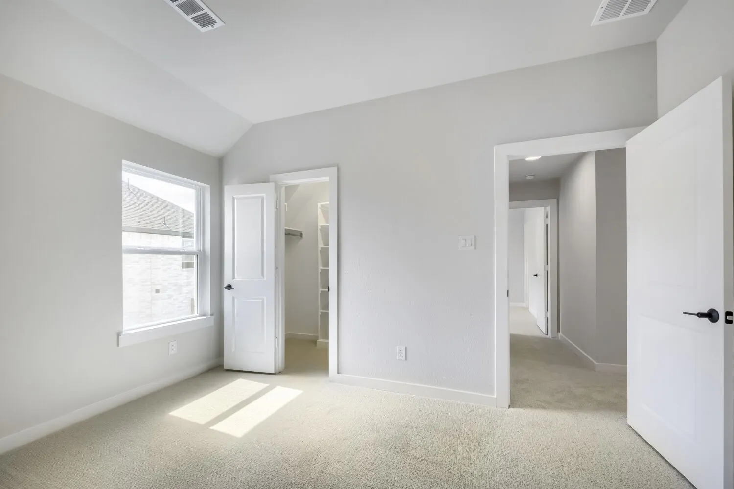 Vaulted ceiling bedroom with light-toned carpet flooring, a double-hung window, and a walk-in closet featuring shelving