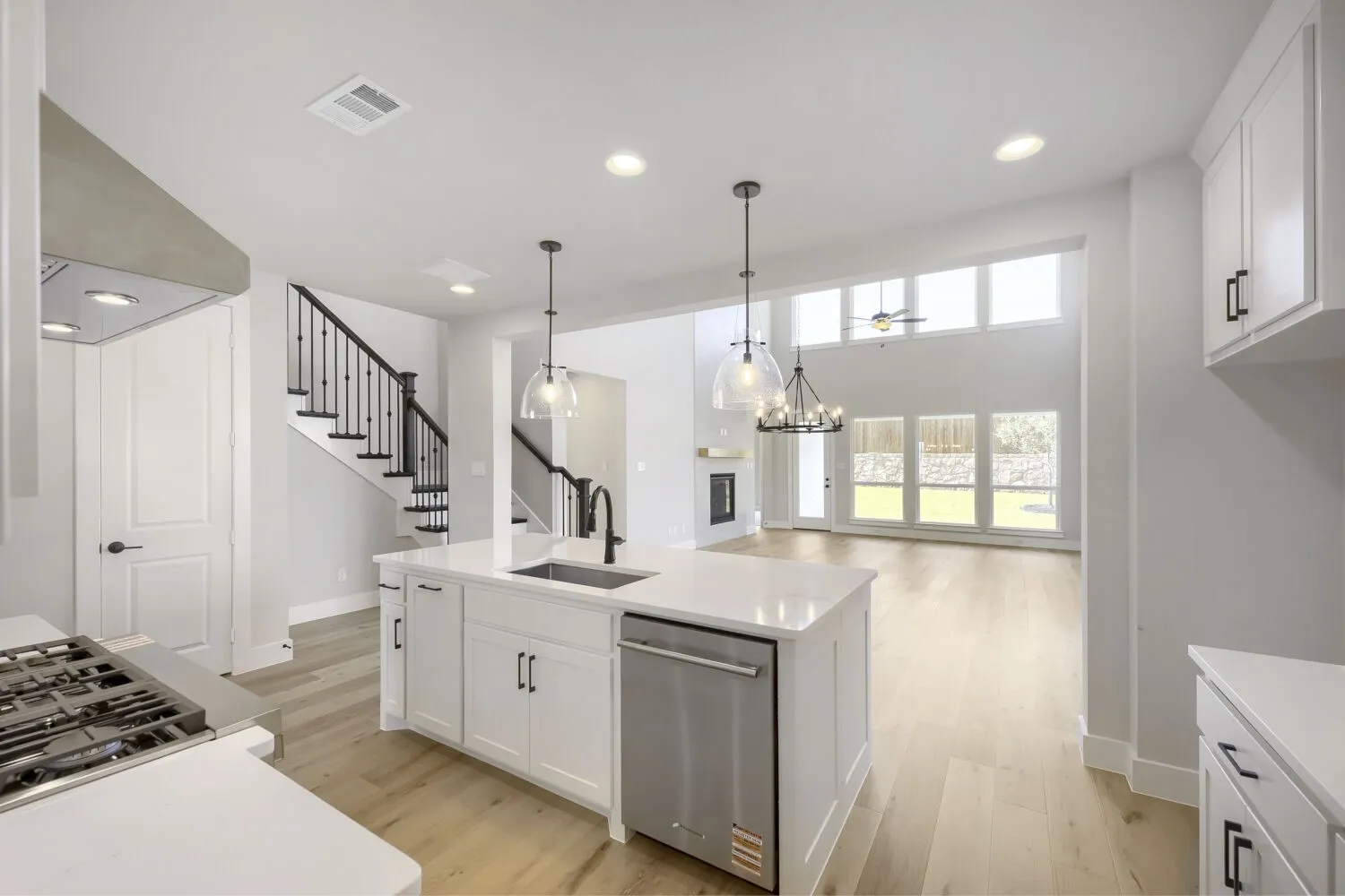 Open-concept kitchen with a large island featuring a built-in sink, stainless steel dishwasher, and pendant lighting